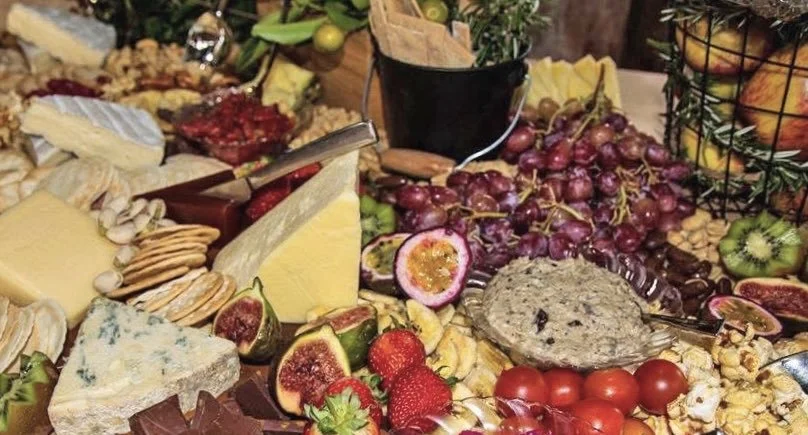 An assorted cheese, fresh strawberries, figs, grapes, cherry tomatoes, and a fruit spread on a buffet table.