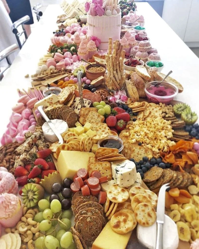 A long table filled with an assortment of desserts, cheeses, fruits, crackers, and sweets arranged for a celebration or party.