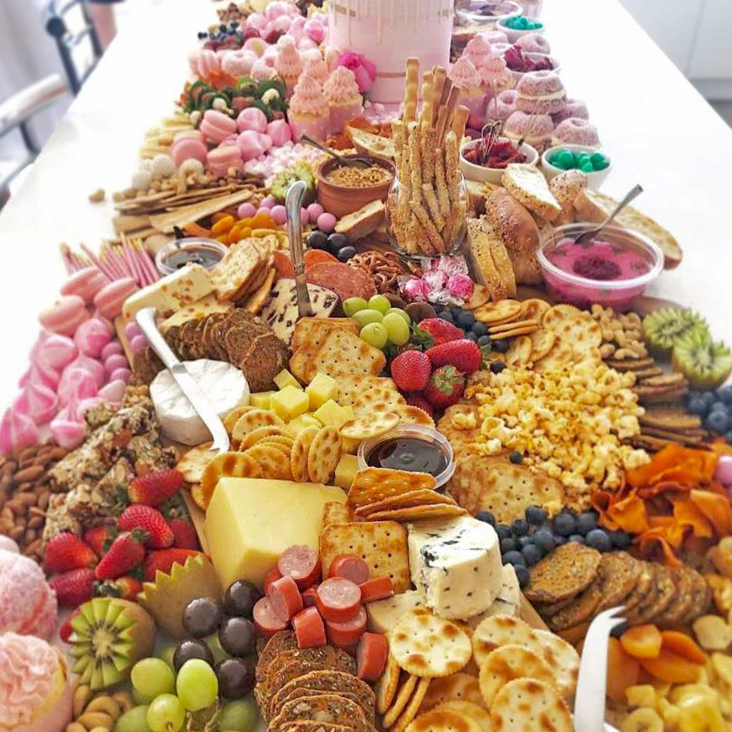A long table filled with a variety of colorful desserts, fruits, cheeses, crackers, and snacks for a celebration or party.
