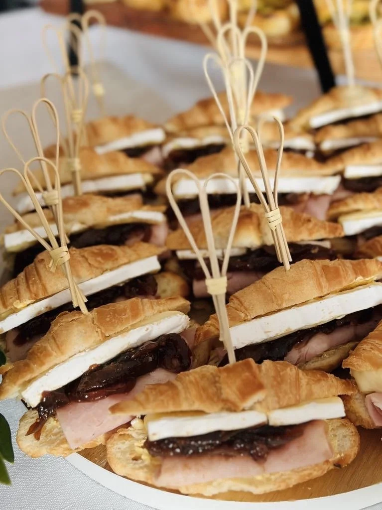 Close-up of assorted croissant sandwiches with ham, cheese, and dark spread, each with a decorative bamboo pick.