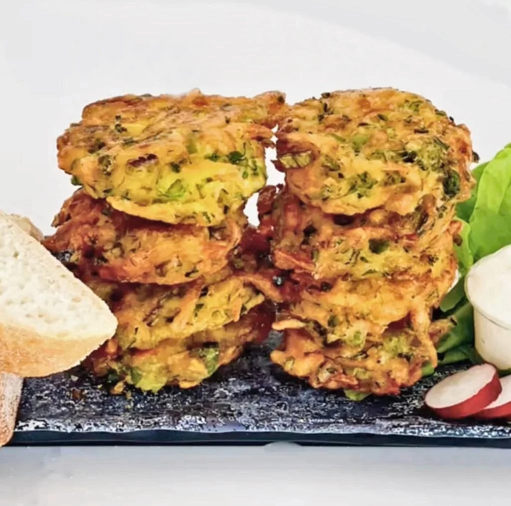 Stacked vegetable fritters with side of sliced radish, lettuce, and dipping sauce on a black serving platter.