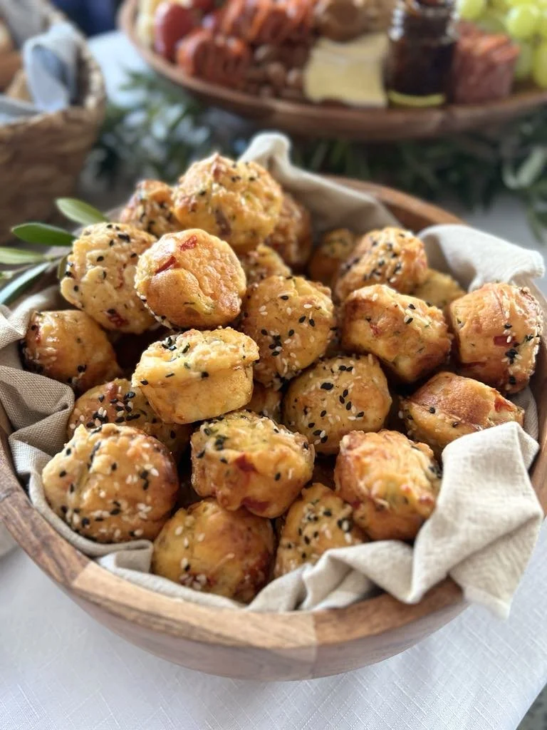 Basket of golden, bite-sized cheese balls sprinkled with black sesame seeds and white salt, served on a cloth-lined wooden bowl.