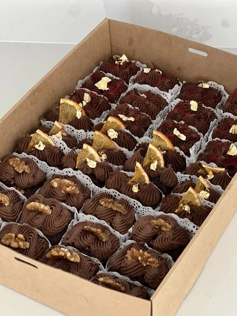 Box of assorted chocolate truffles topped with nuts, citrus slices, and gold leaf.