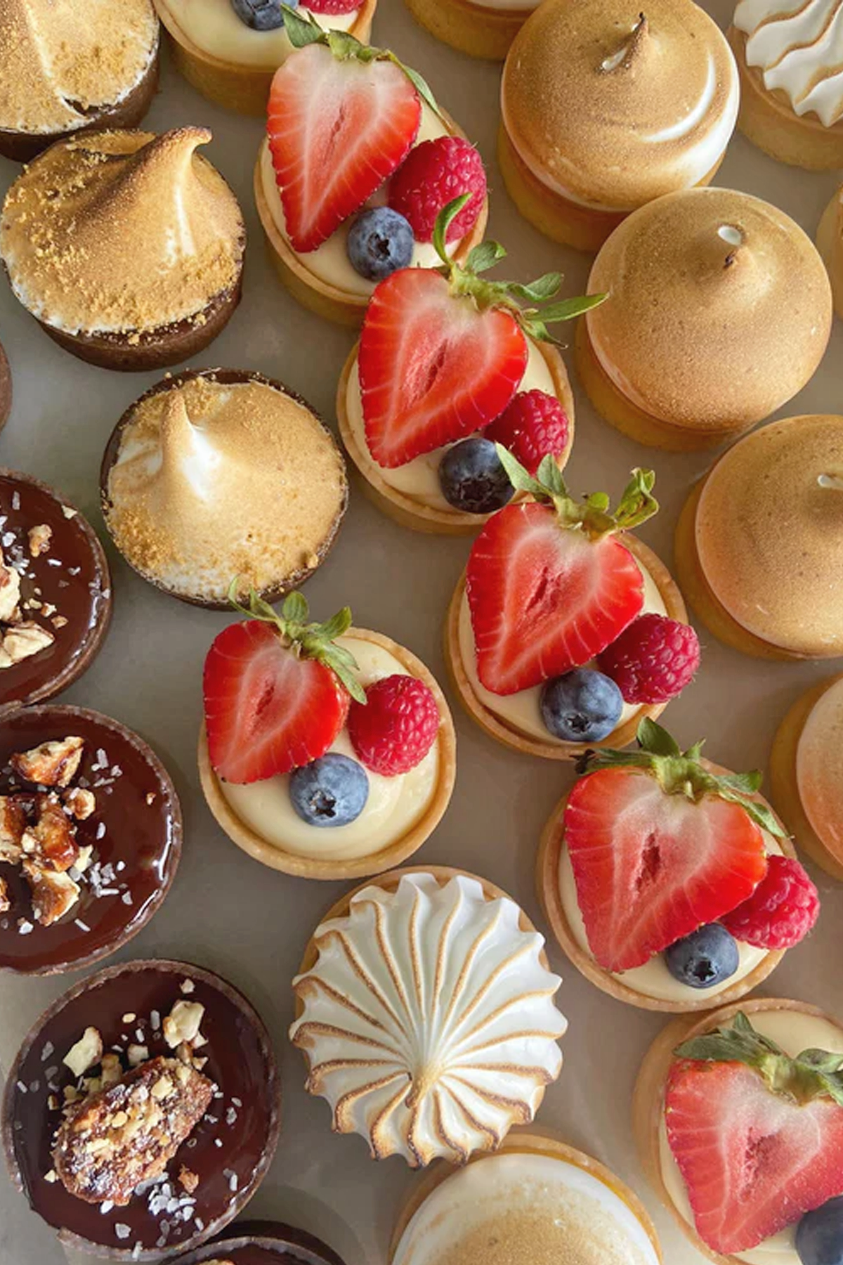 Assorted mini desserts including fruit-topped tarts, chocolate cups, and meringue treats