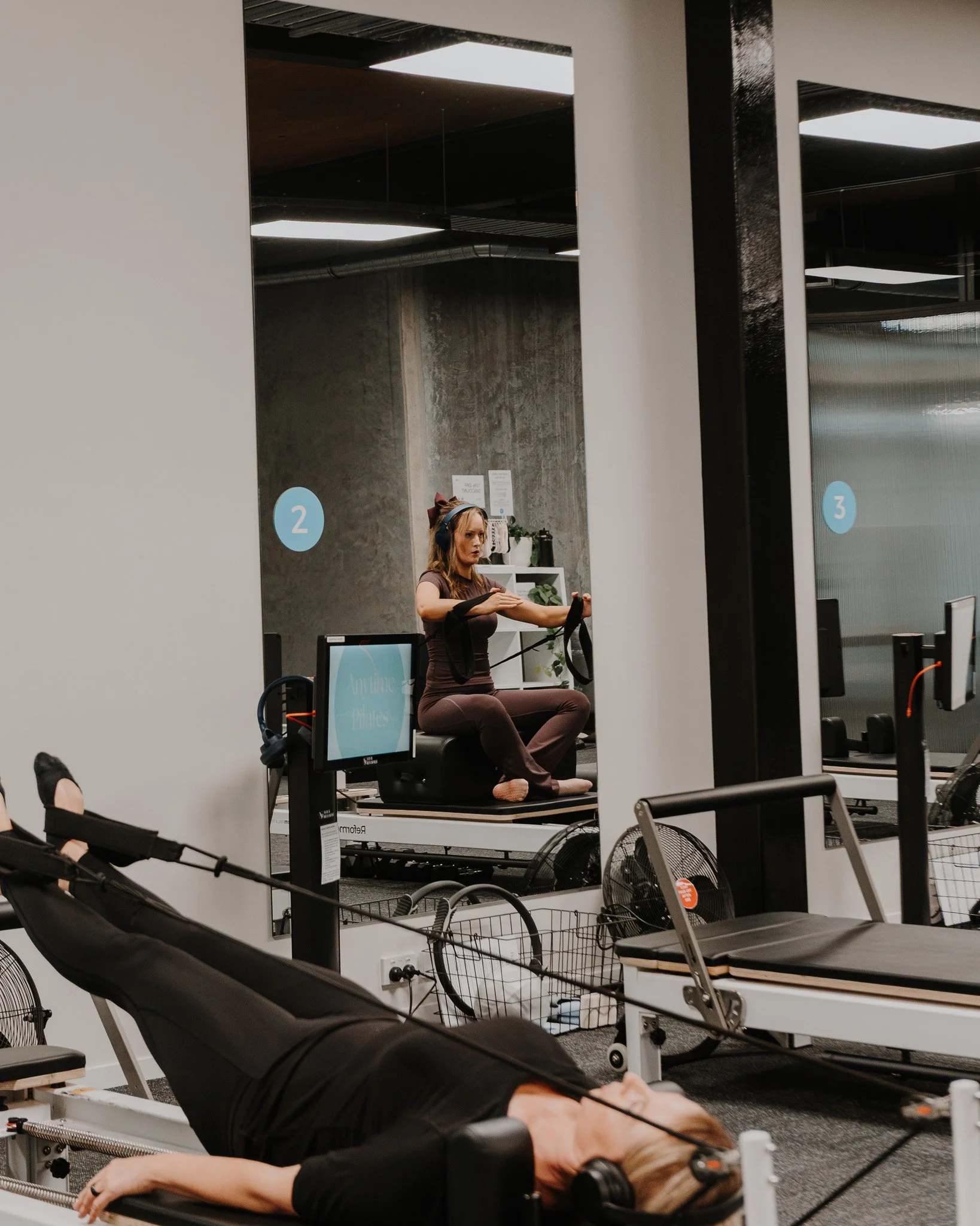 Two woman with headphones on pilates reformers in studio