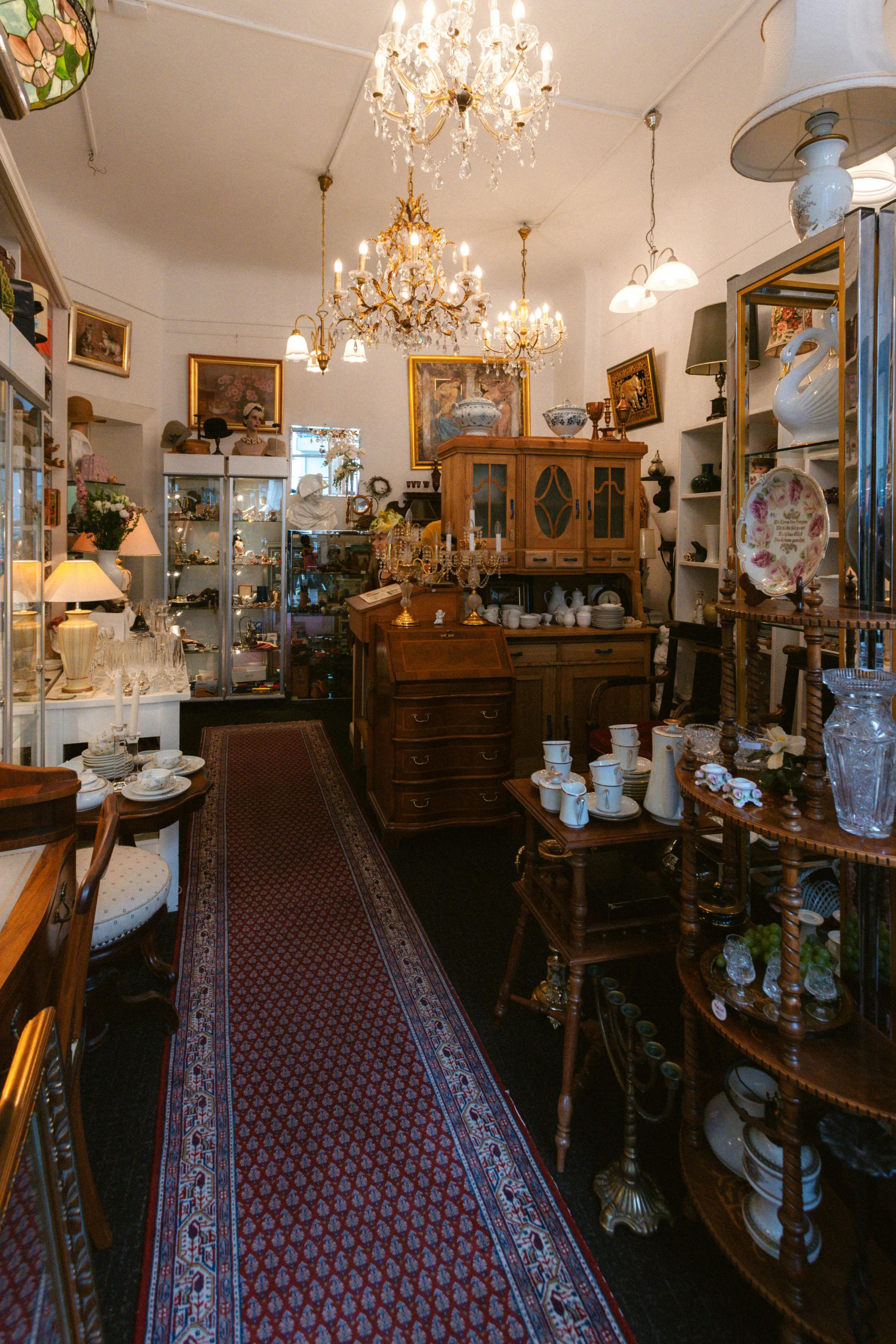 Innenansicht eines Antiquitätengeschäfts mit antiken Möbeln, Geschirr, Dekorationsgegenständen, Kronleuchtern und Lampen.