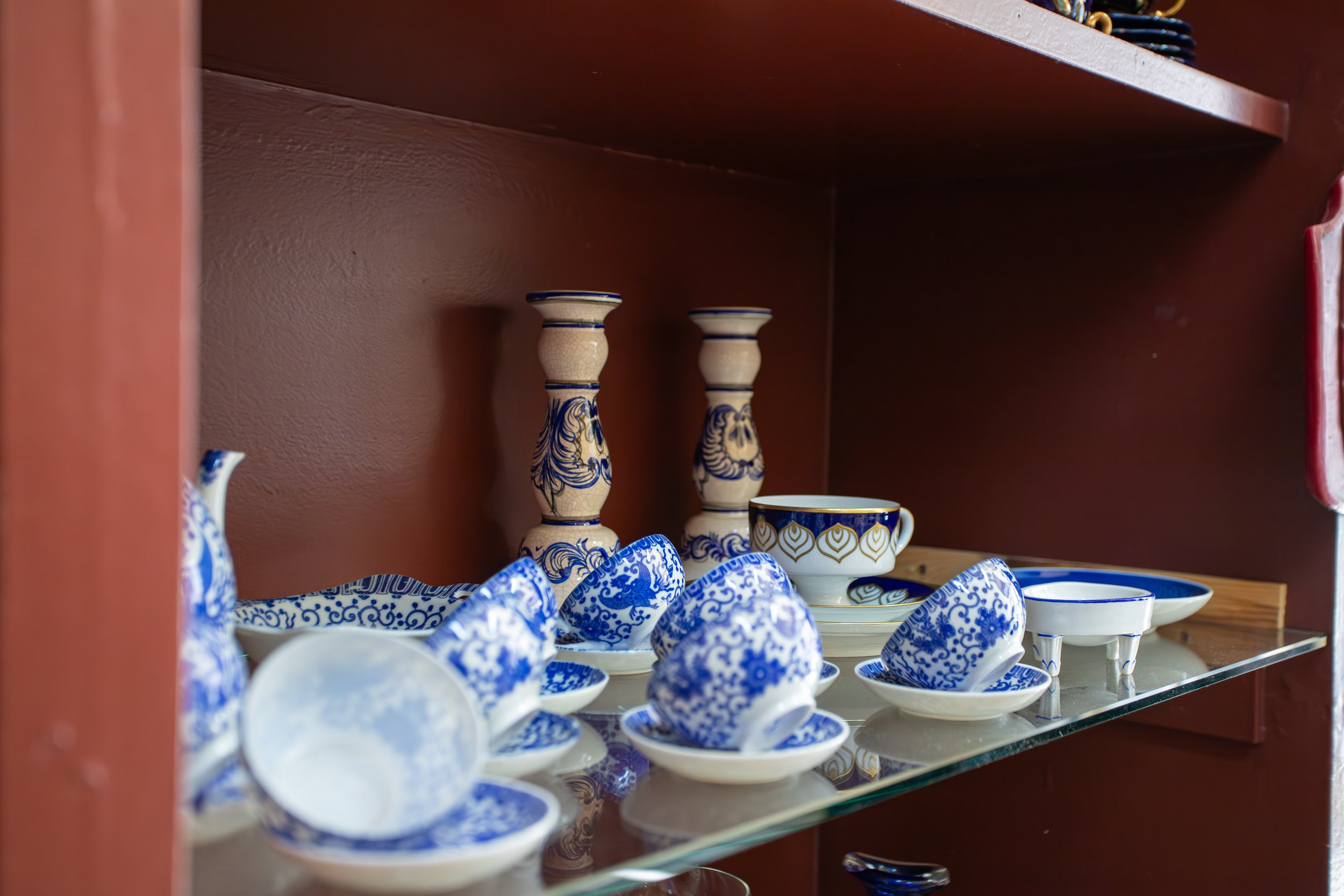 Bunte keramische Geschirrteile, darunter Schalen, Tassen und zwei Kerzenhalter, in einer Vitrine