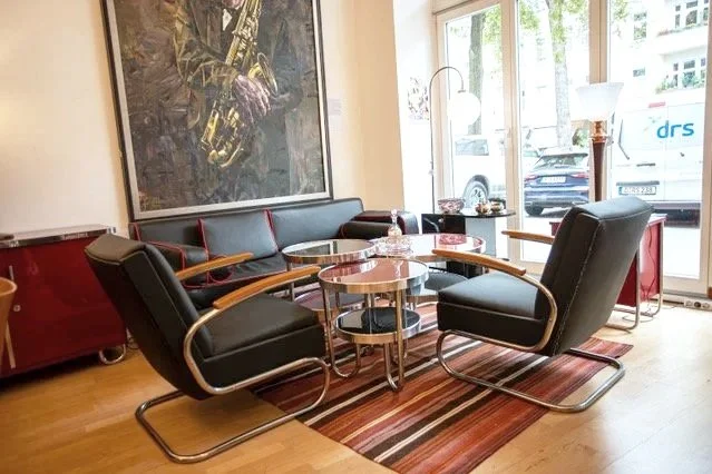 Sitzbereich in einem Raum mit schwarzen Sesseln, Couchtisch, rotem Schrank, großer Wandkunst und Blick auf die Straße durch große Fenster