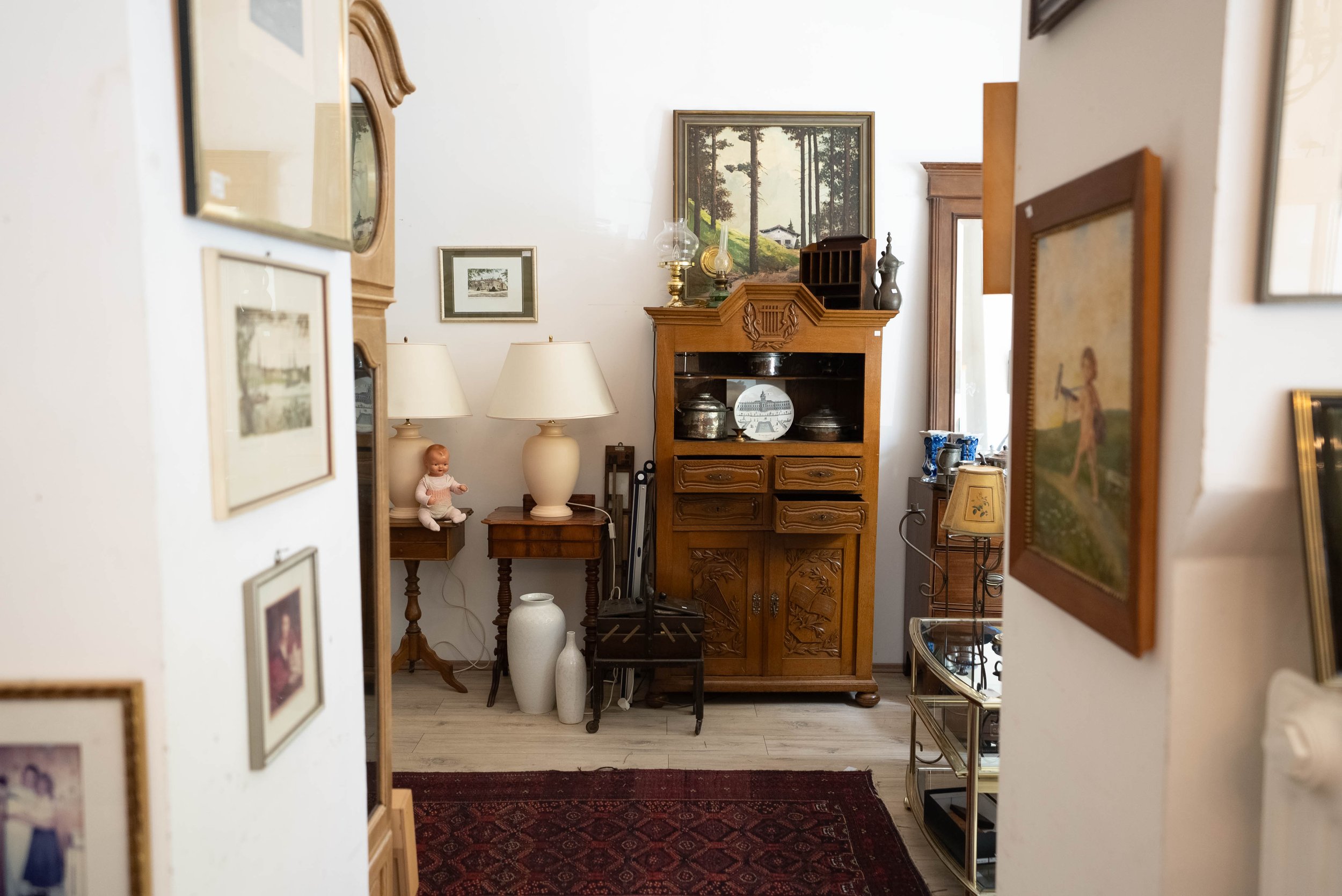 Blick in ein Wohnzimmer mit antiken Möbeln, Gemälden an der Wand, Lampen, Dekorationsgegenständen und einem roten Teppich.