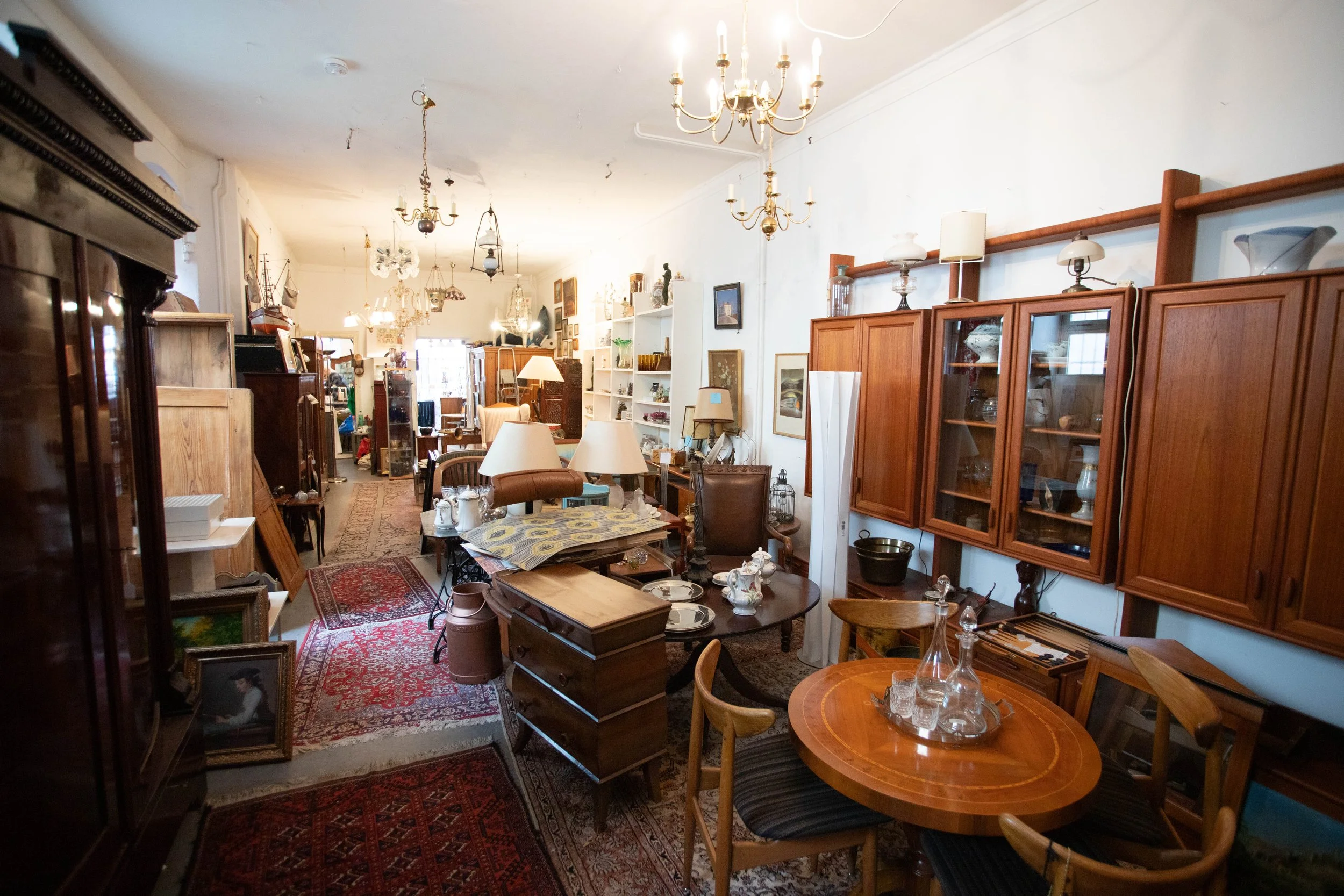 Ein Raum voller alter Möbelstücke, Vasen, Lampen und Dekorationsgegenstände in einem Antiquitätengeschäft.