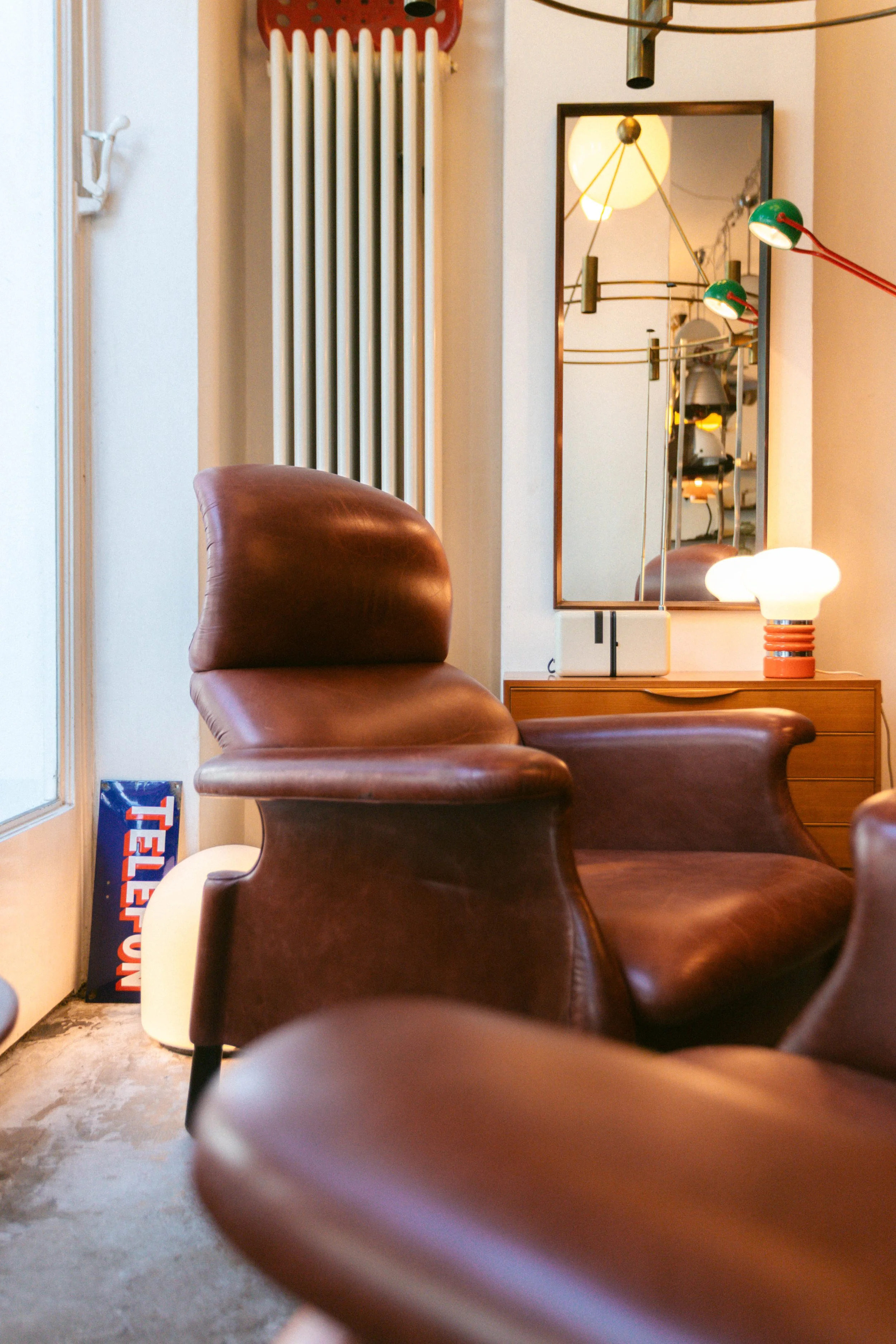 Gemütliches Wohnzimmer mit braunen Ledersesseln, einem großen Spiegel an der Wand, einem Tisch mit einer Lampe, und einem Wandheizkörper.