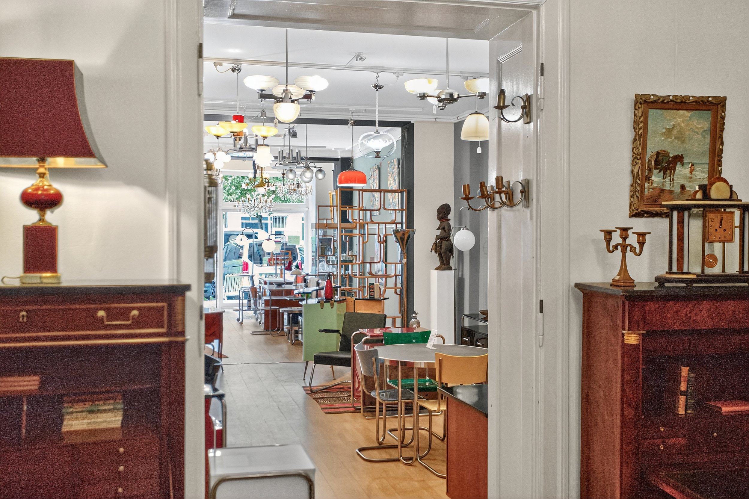 Innenansicht eines Cafés mit Vintage- und Mid-Century-Möbeln, mehreren Deckenlampen, dekorativen Objekten und einem Blick auf die Straße draußen.