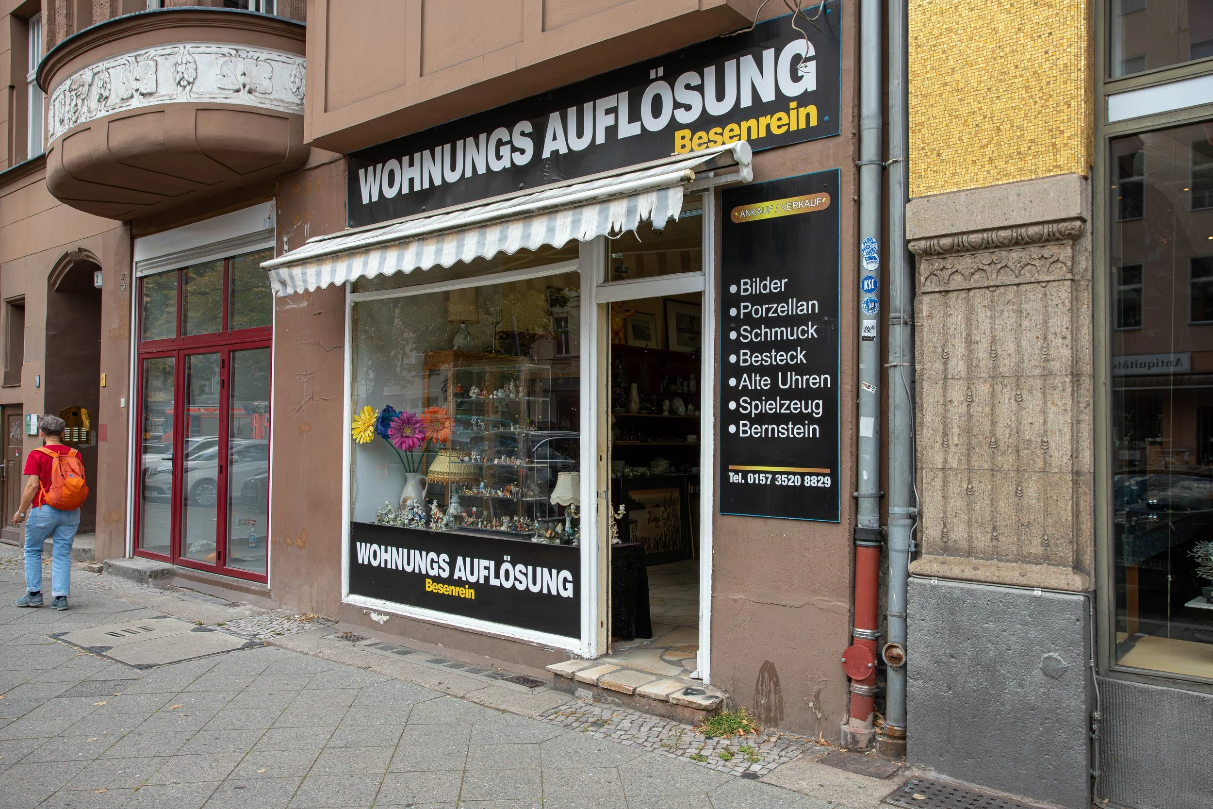 Schaufenster eines Second-Hand-Ladens mit Verkauf von Figuren, Porzellan, Schmuck, Besteck, alten Uhren, Spielzeug und Bernstein. Das Geschäft heißt 'Wohnungsauflösung' in Bessenrein.