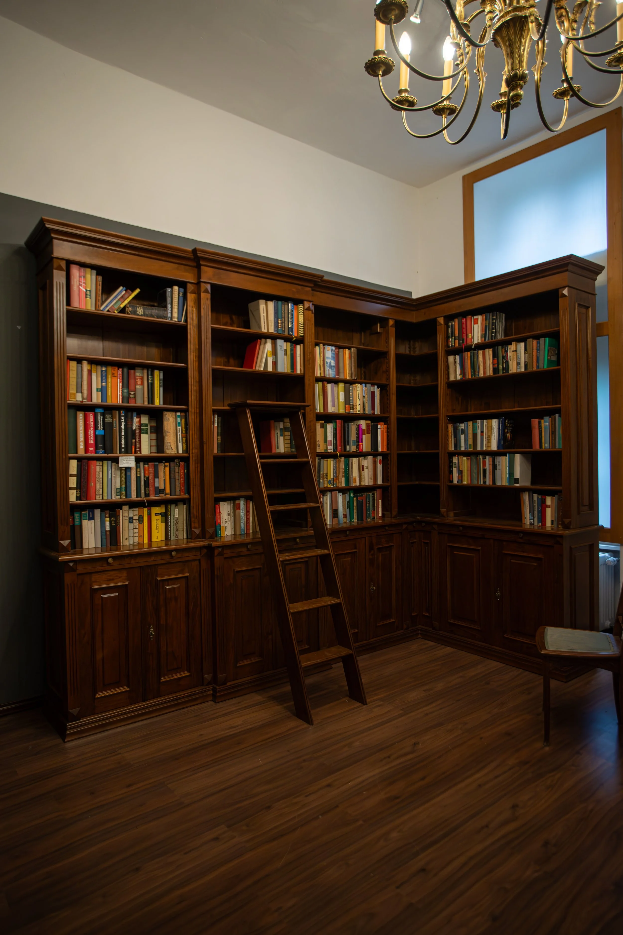 Große Holzbibliothek mit vollgestellten Bücherregalen, Leiter, Stuhl und Kamin