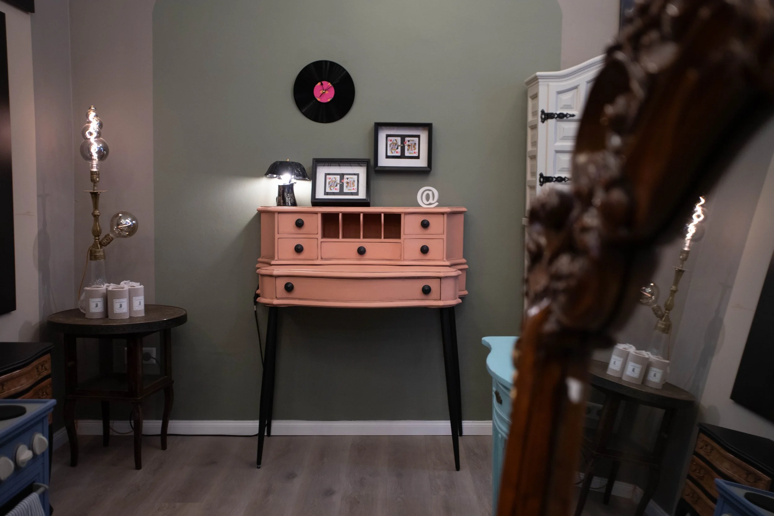 Innenraum eines Wohnzimmers mit einer grünen Wand, einem pinken Schreibtisch mit schwarzen Knöpfen, Wanddekoration, einem schwarzen Lampen und weiteren Möbeln.