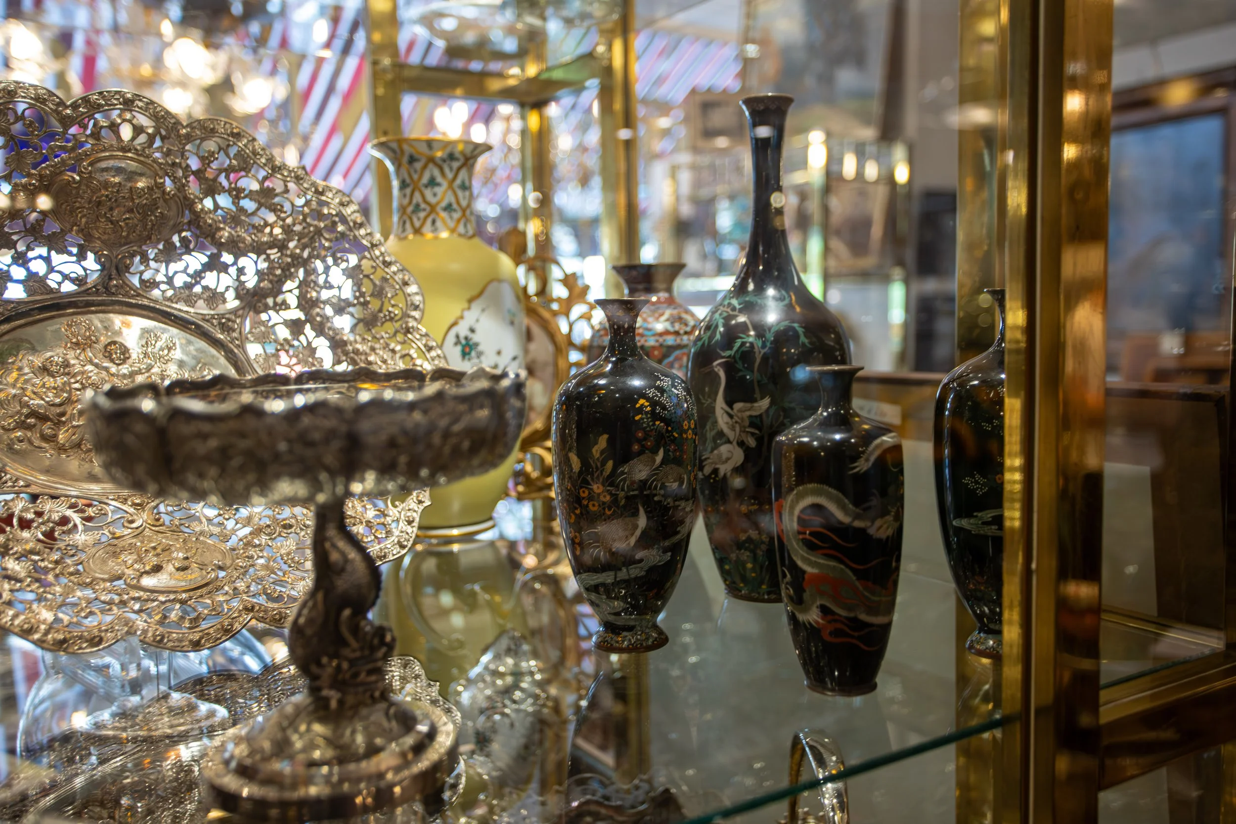 Antike Vasen und silberne Dekorationsgegenstände in einem Glasschaukasten in einem Antiquitätengeschäft.