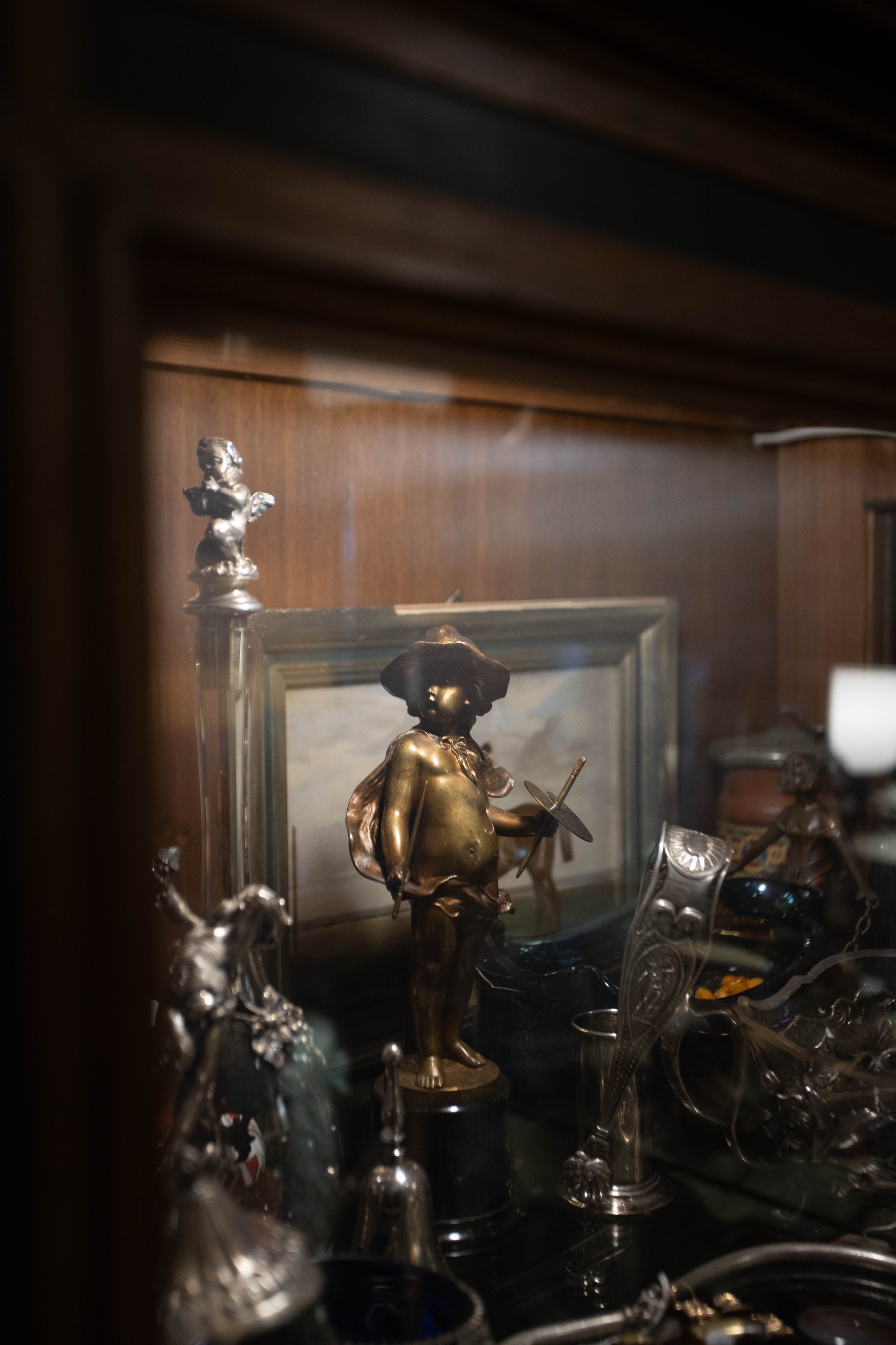 Ansicht von kunstvollen Skulpturen und Silbergegenständen in einem Schaukasten, bei denen ein figuraler Bronze- oder Metallkopf und eine Figur mit Hut und Pinsel im Zentrum sichtbar sind.