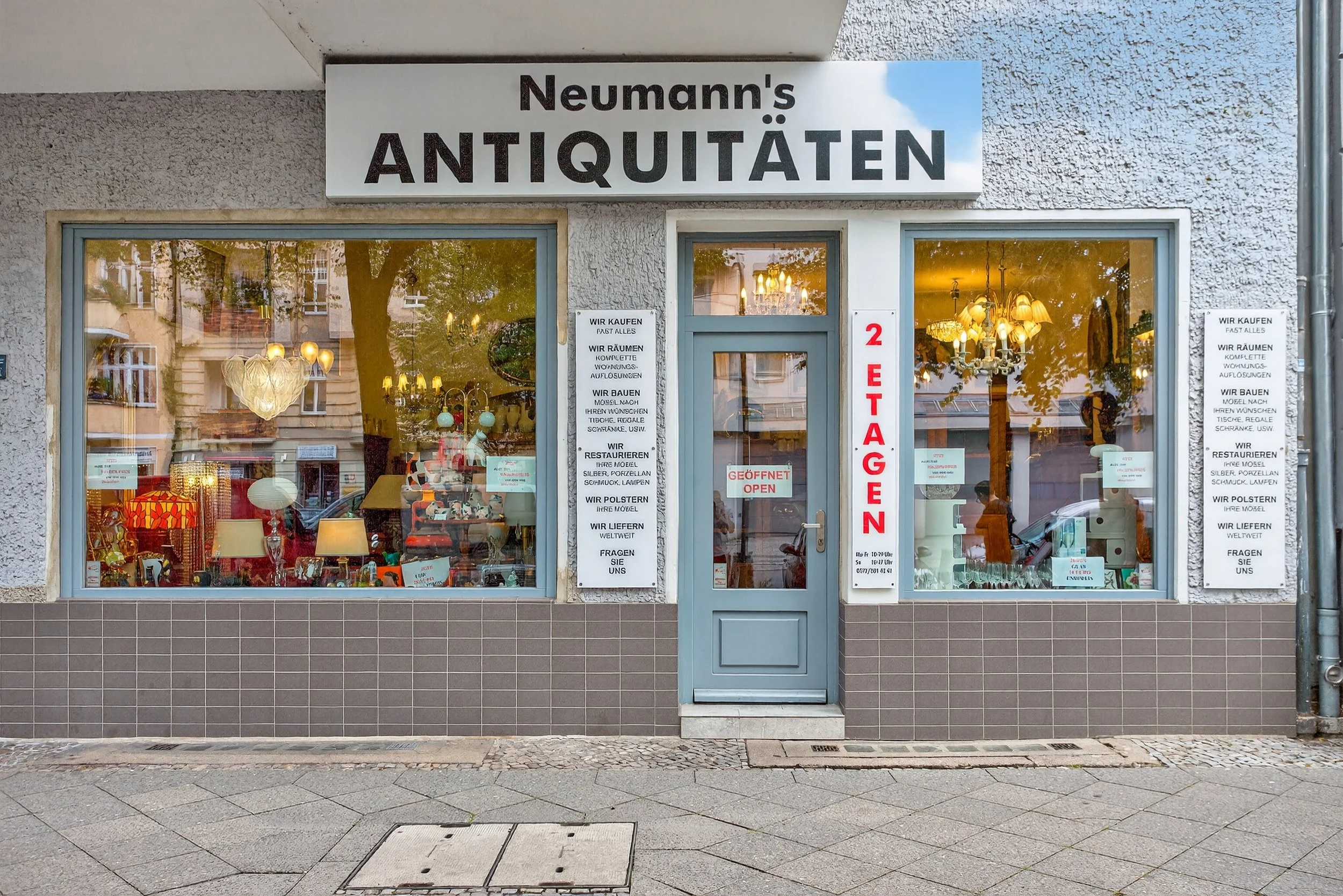 Schaufenster eines Antiquitätenladens mit dem Namen "Neumann's Antiquitäten". Das Geschäft hat eine blaue Tür mit einem roten Schriftzug "2 ETAGEN" und "GEÖFFNET" in der Tür. Im Fenster sind verschiedene antike Möbel und Lampen zu sehen.