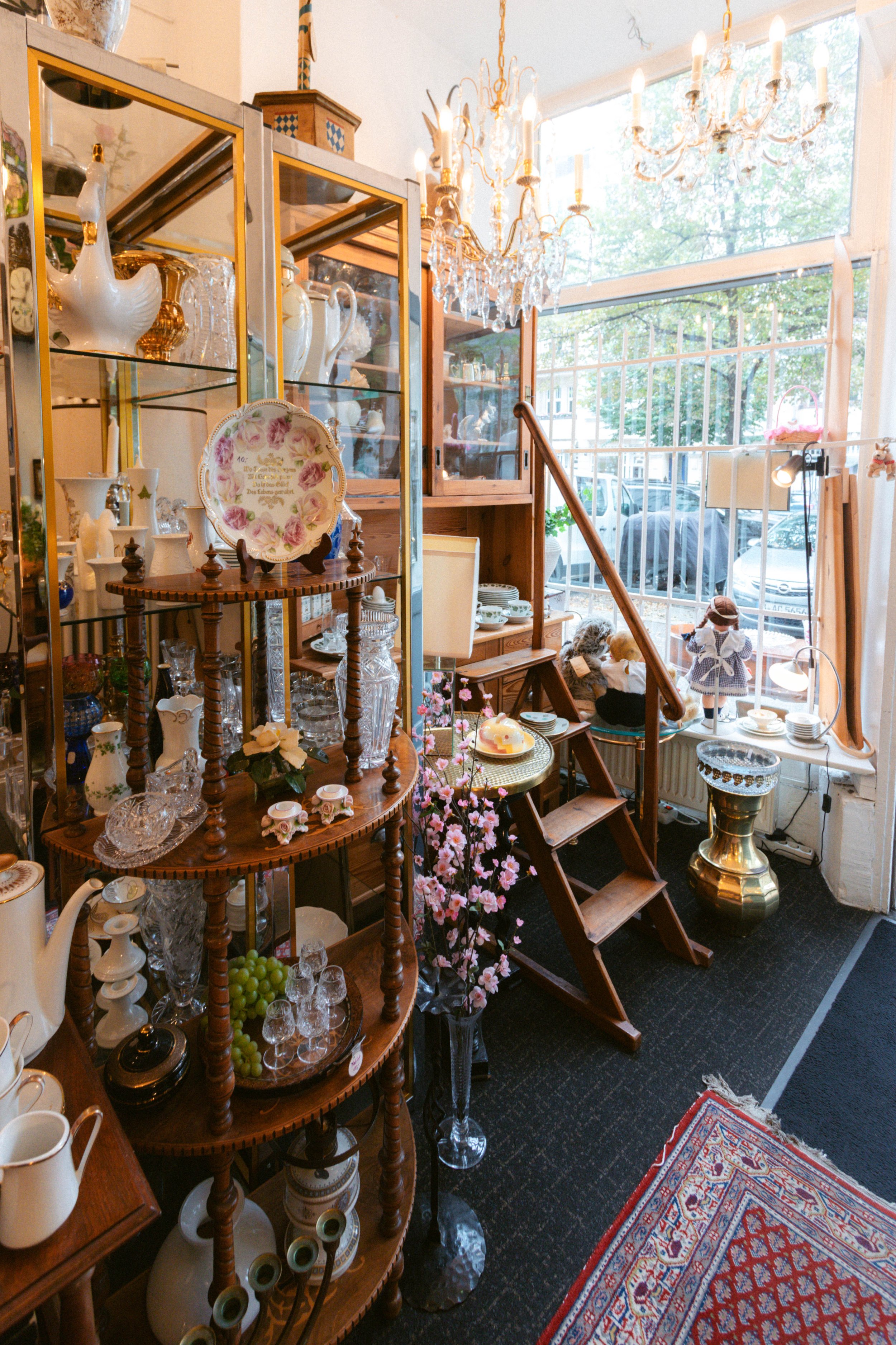 Innenraum eines Antiquitätengeschäfts mit Glastresen, Kerzenleuchtern, Porzellan, Keramik und Dekoartikeln, große Fenster mit Blick nach draußen.