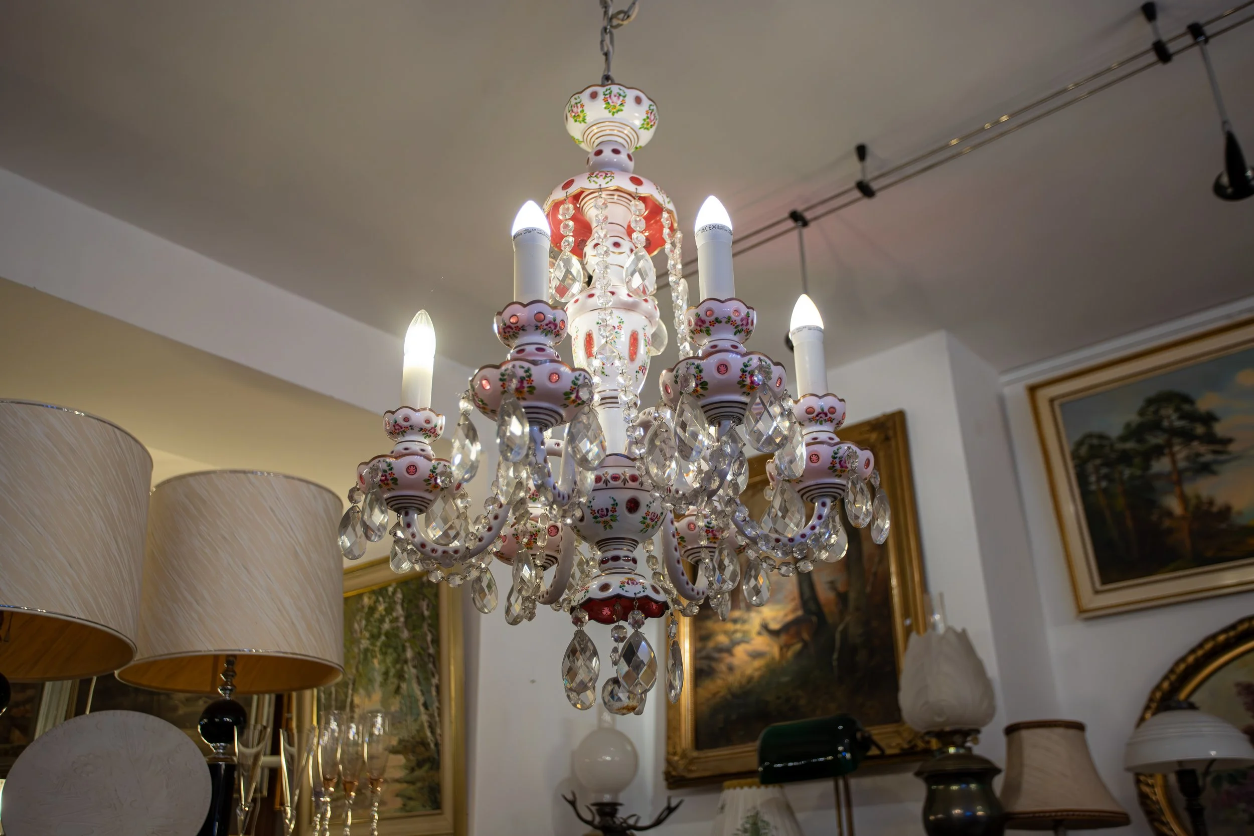 Hängeleuchte mit Kristallanhängern in einem Einrichtungsraum, umgeben von Bildern und Lampen.