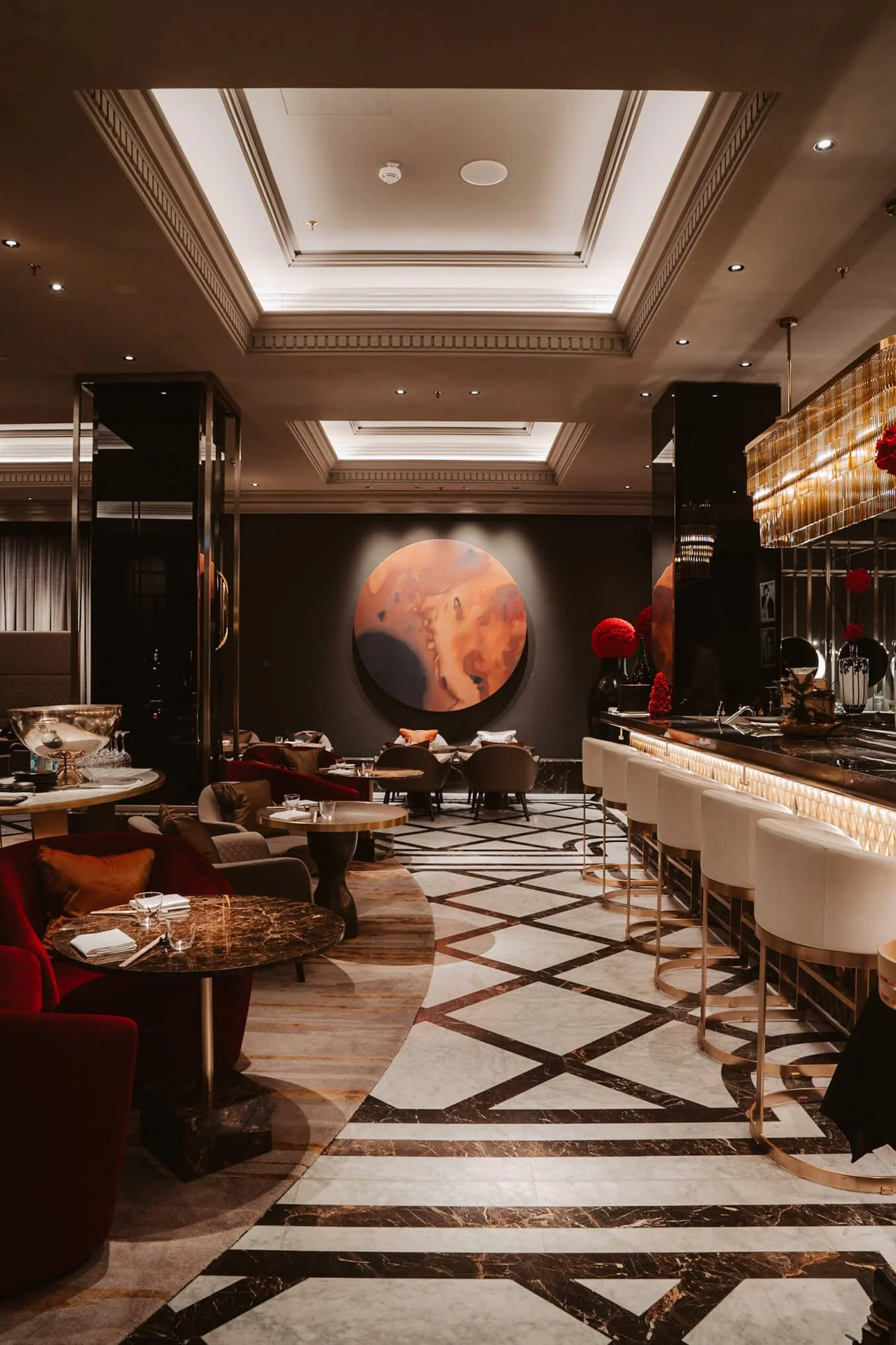 Elegant restaurant interior with marble flooring, modern furniture, a bar area, and abstract artwork on the dark wall.