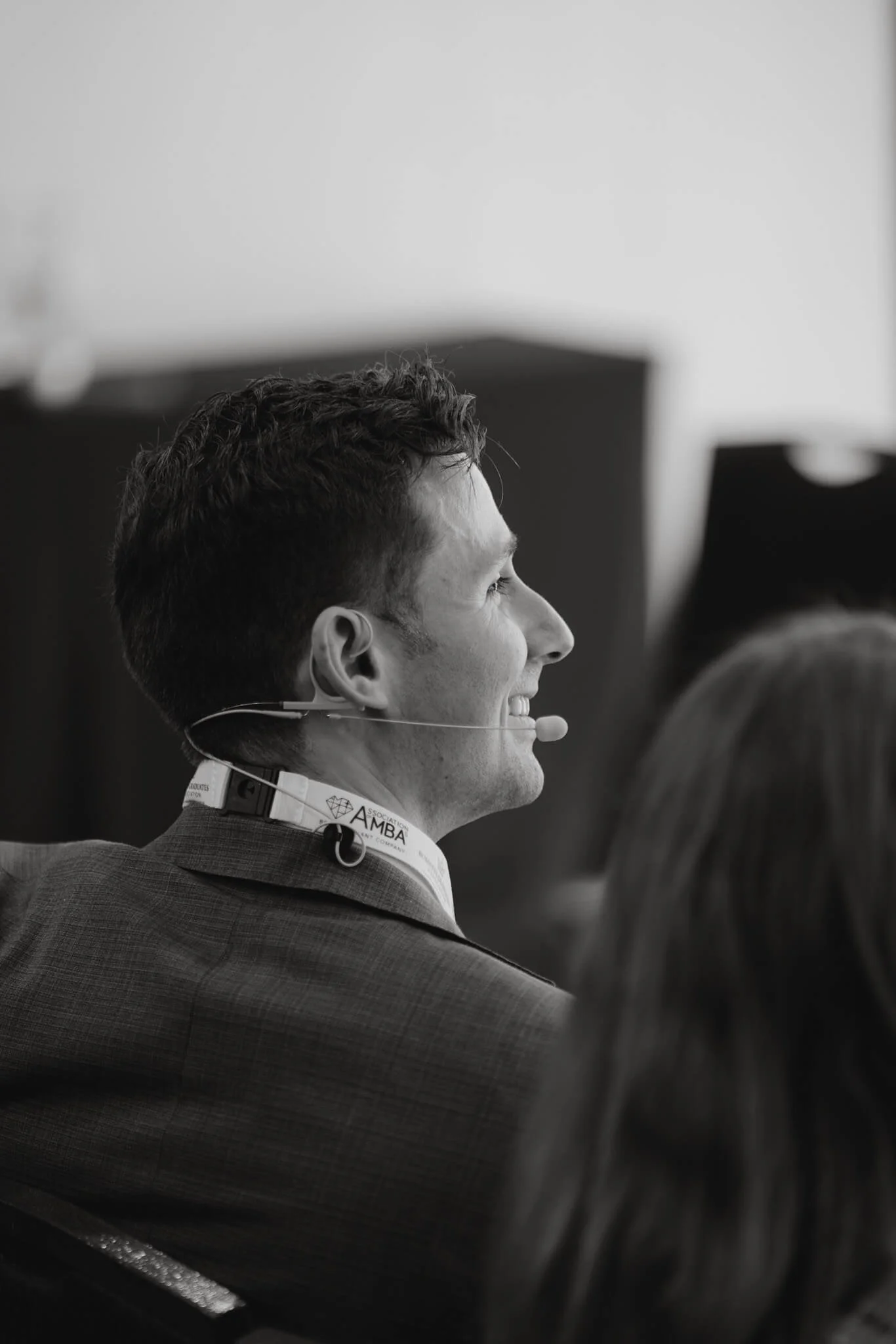 A man in a suit smiling in profile while wearing a headset at a conference.