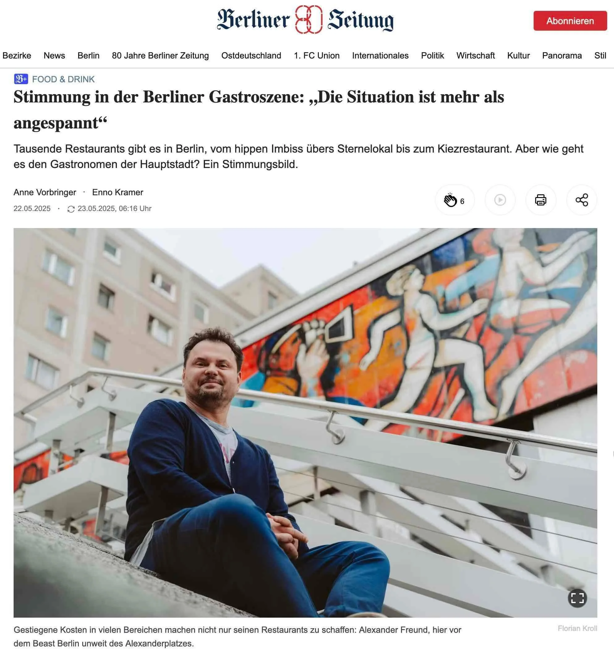 Ein Mann sitzt auf einer Treppe vor einem Graffiti an einer Wand, im Hintergrund ein Hochhaus. Er trägt eine dunkle Jacke und Jeans und hat dunkle, kurze Haare.