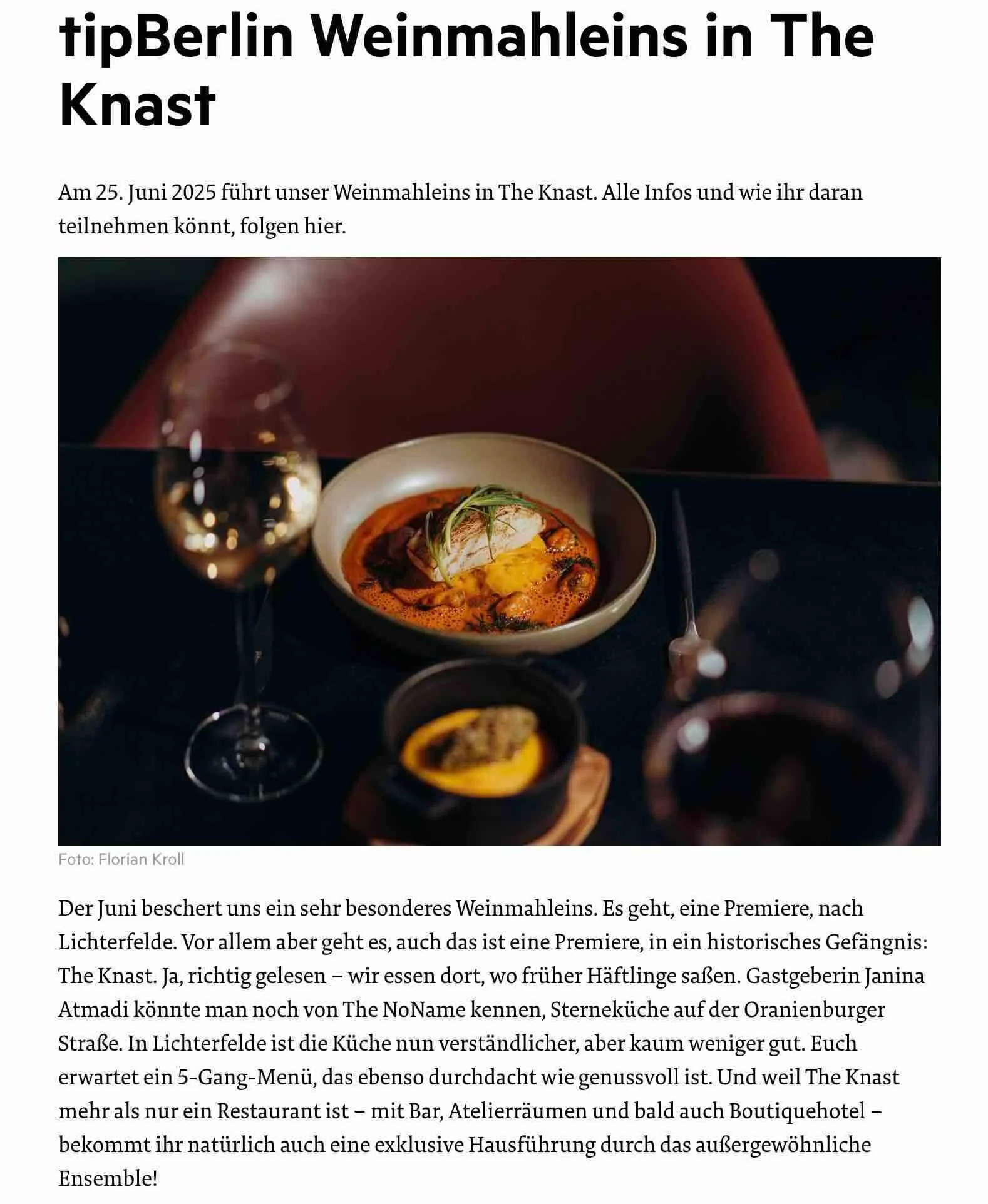 Ein Bild von einem Teller mit einem Gericht, vermutlich Meeresfrüchten, garniert mit Kräutern, neben einem Glas Weißwein auf einem dunklen Tisch. Im Hintergrund ist der Teil eines Rotweinglases sichtbar.
