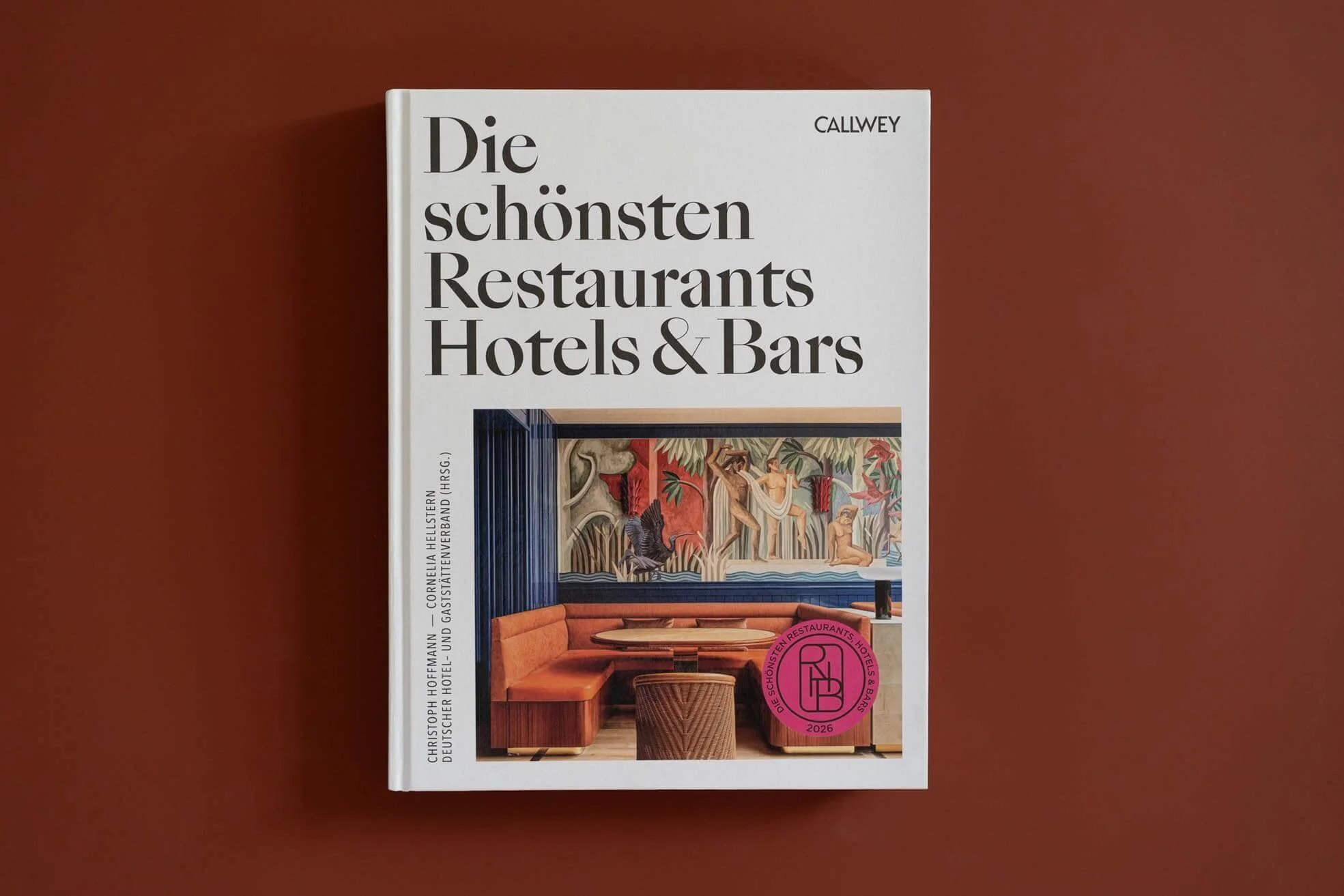 Buchcover mit deutschem Titel "Die schönsten Restaurants Hotels & Bars", zeigt eine stilvolle Innenraumgestaltung mit Wandkunst, Rattan-Möbeln und einem roten Sofa.