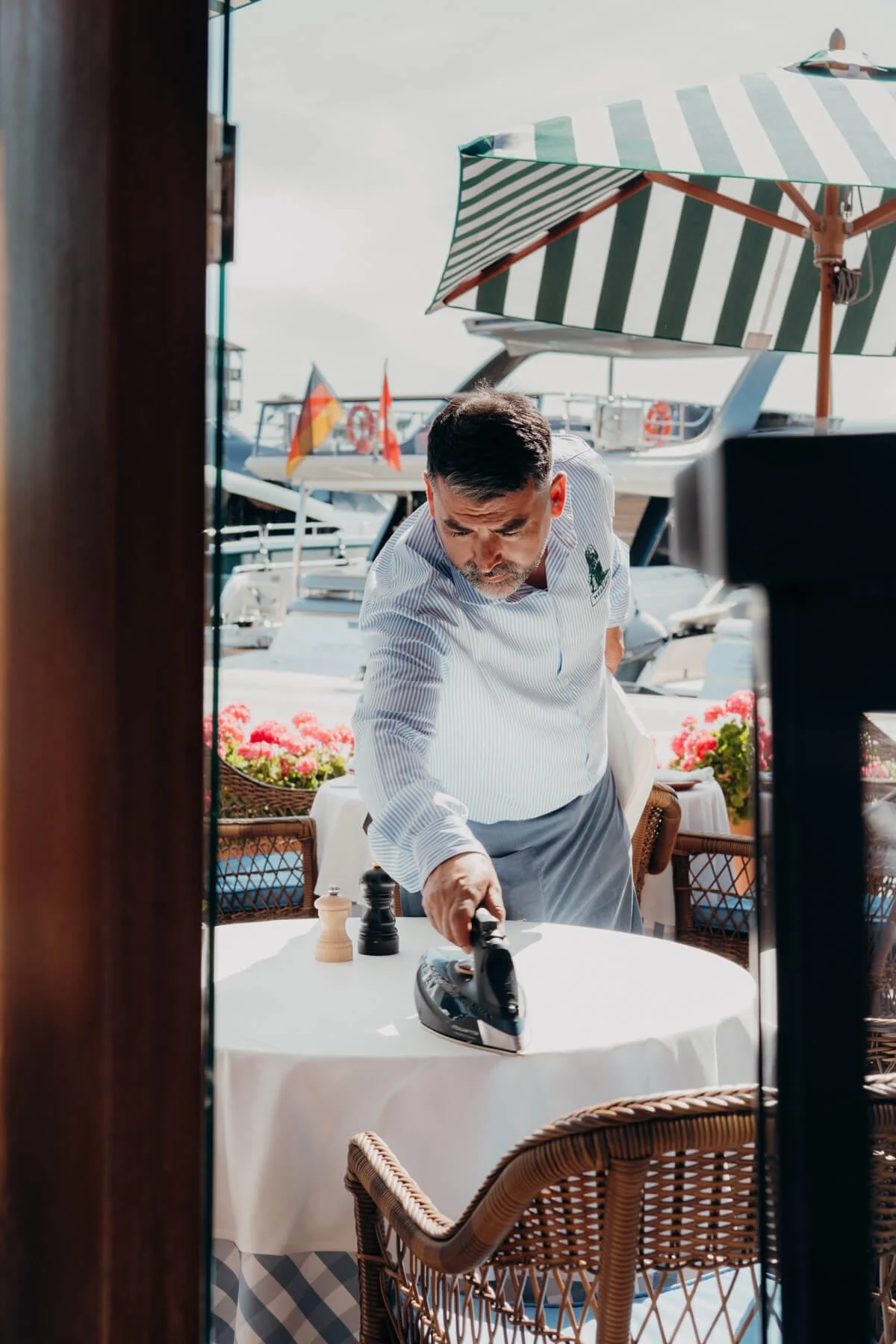 Mann im Restaurant bügeln an einem Tisch auf einer Terrasse mit Blick auf Boote im Hafen