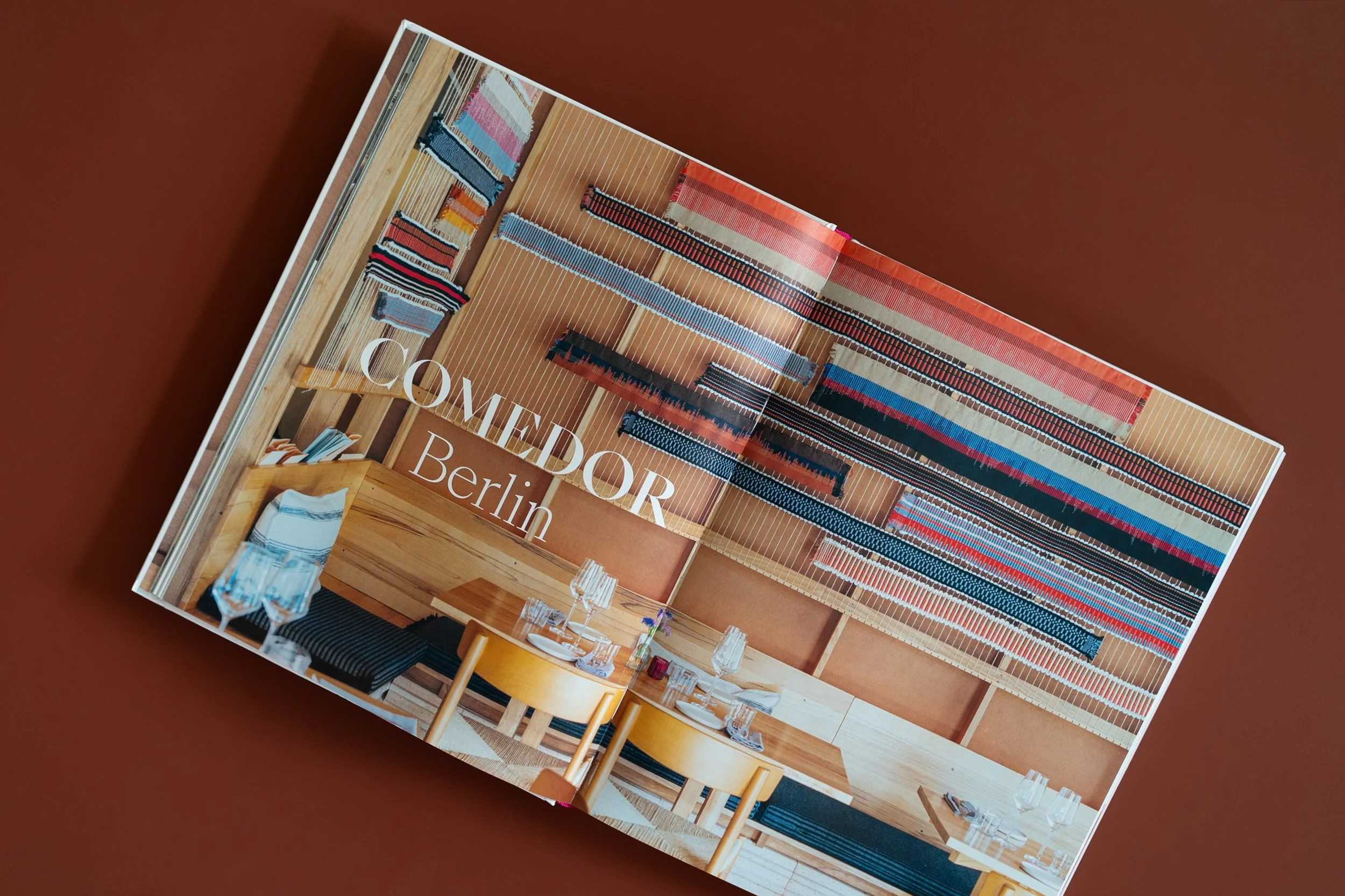 Ein lebendiger Inneneinrichtungs-Katalog mit farbenfrohen Stoffmustern, Holzmöbeln und gedecktem Esstisch, auf braunem Hintergrund.