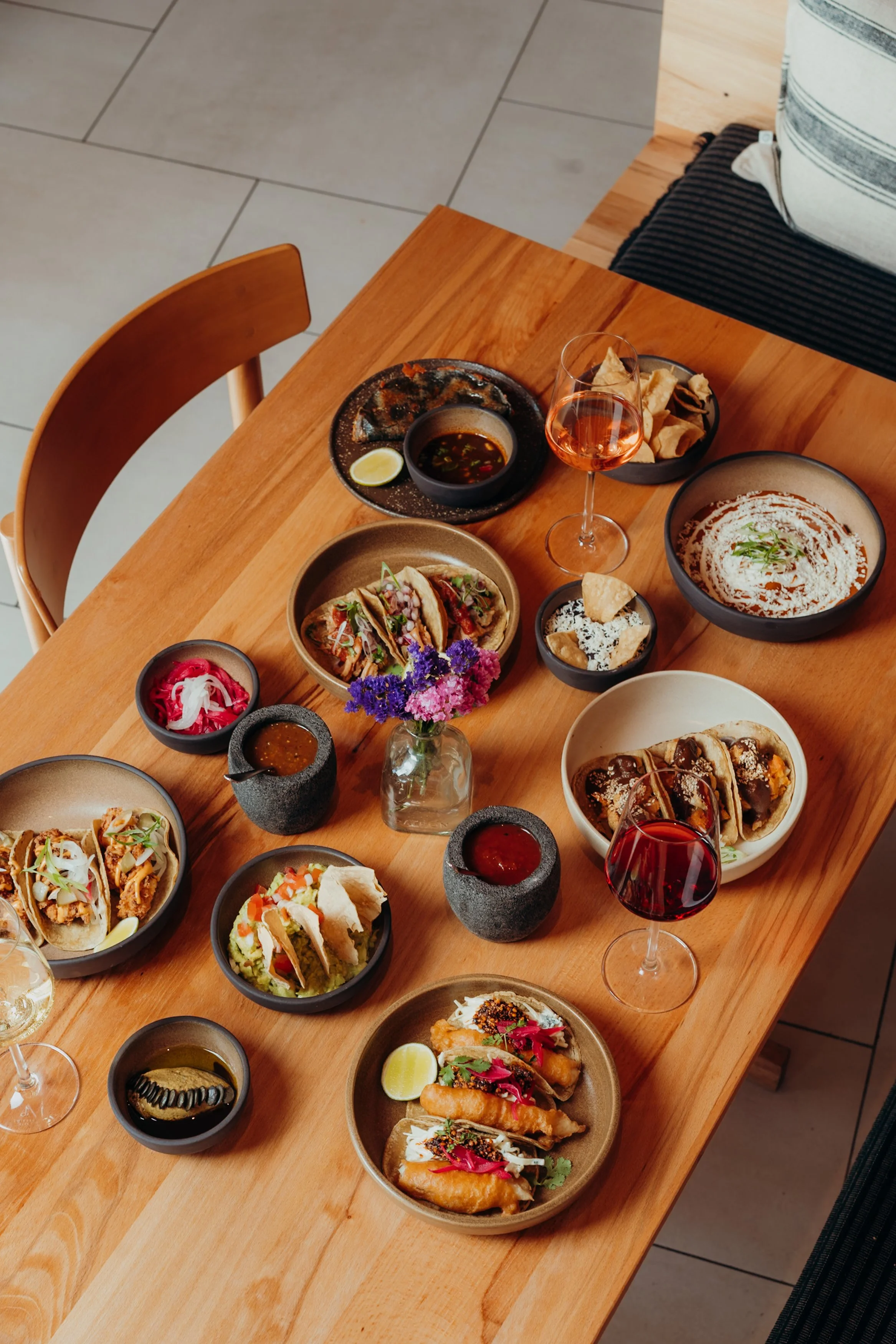Verschiedene mexikanische Gerichte, Tacos, Chilaquiles, Saucen, und Getränke auf einem Holztisch in einem Restaurant.