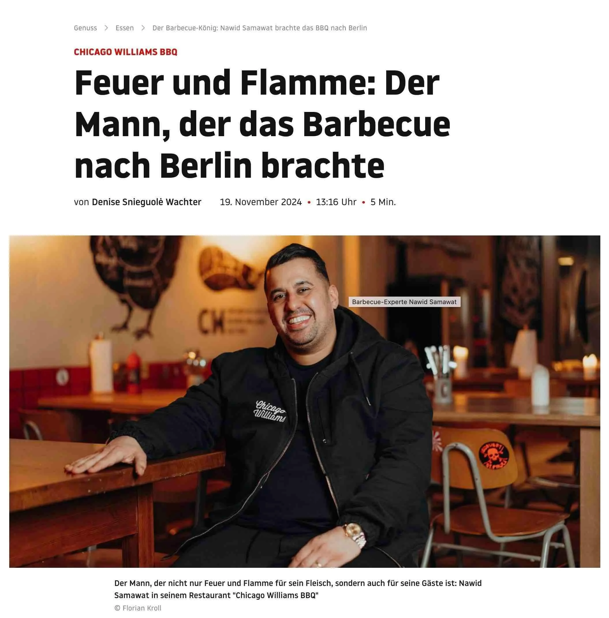 Ein Mann sitzt an einem Holztresen in einem Restaurant namens "Chicago Williams BBQ". Er trägt eine schwarze Jacke mit einem Logo auf der linken Brust. Im Hintergrund sind amerikanische Flaggen und verschiedene Dekorationen sichtbar.
