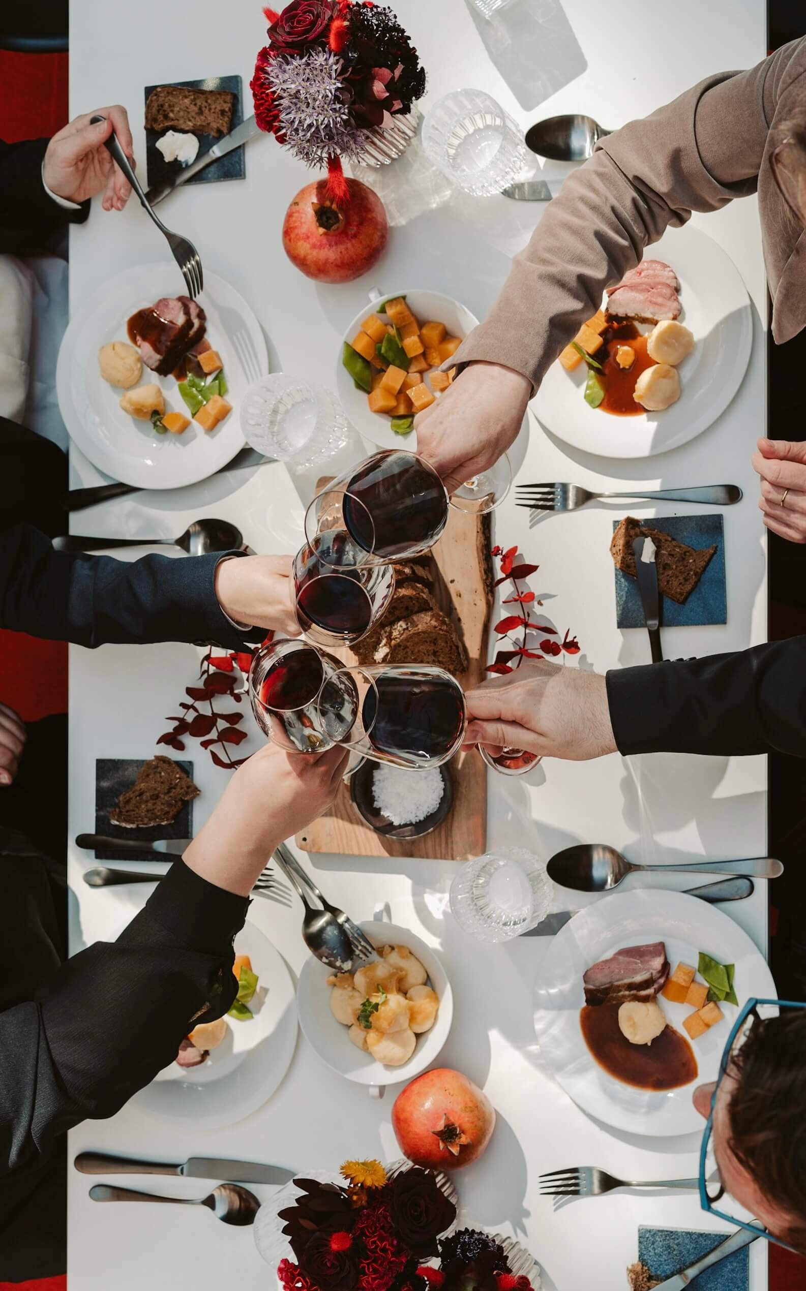 Eine festlich gedeckte Tafel mit verschiedenen Speisen, Wein und Dekorationen wie Blumen und Äpfeln, bei einem gemeinsamen Essen.