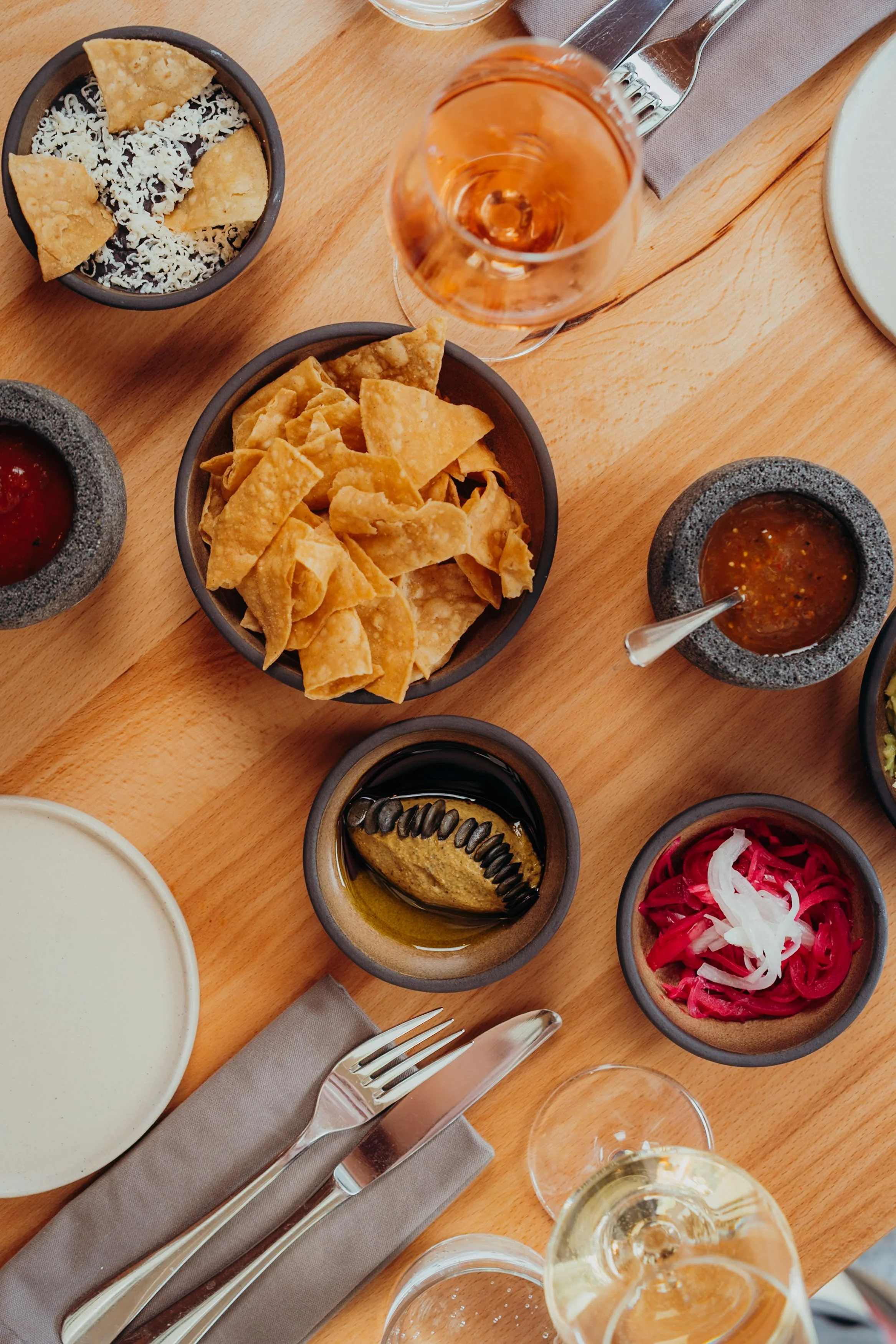 Tisch mit mexikanischen Speisen und Getränken, einschließlich Nachos, Guacamole, Salsa, rotem Mais-Salat, Pickles, Rotwein, Weißwein und Wasser.