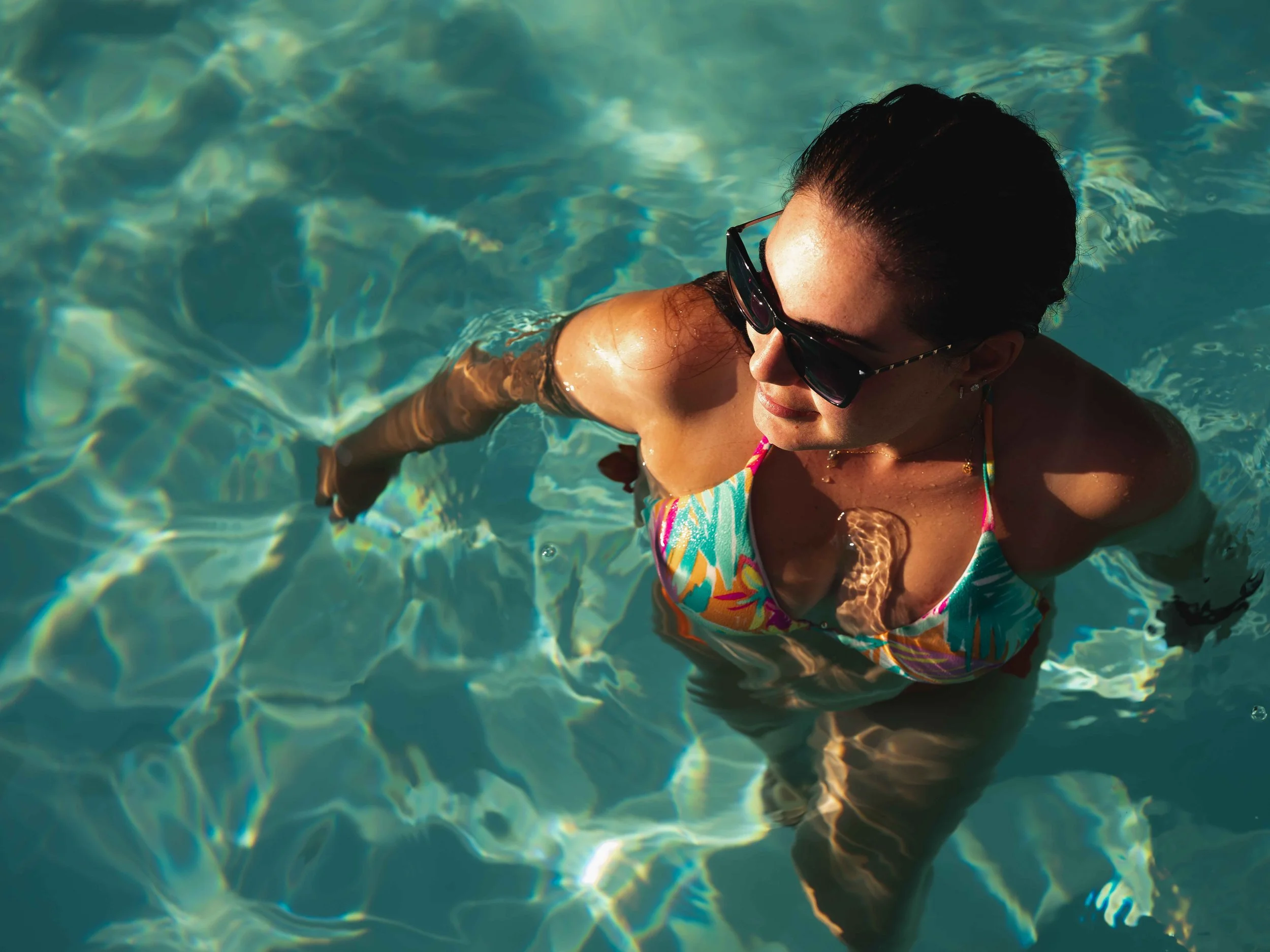Donna con occhiali da sole nuota in piscina, vista dall'alto.