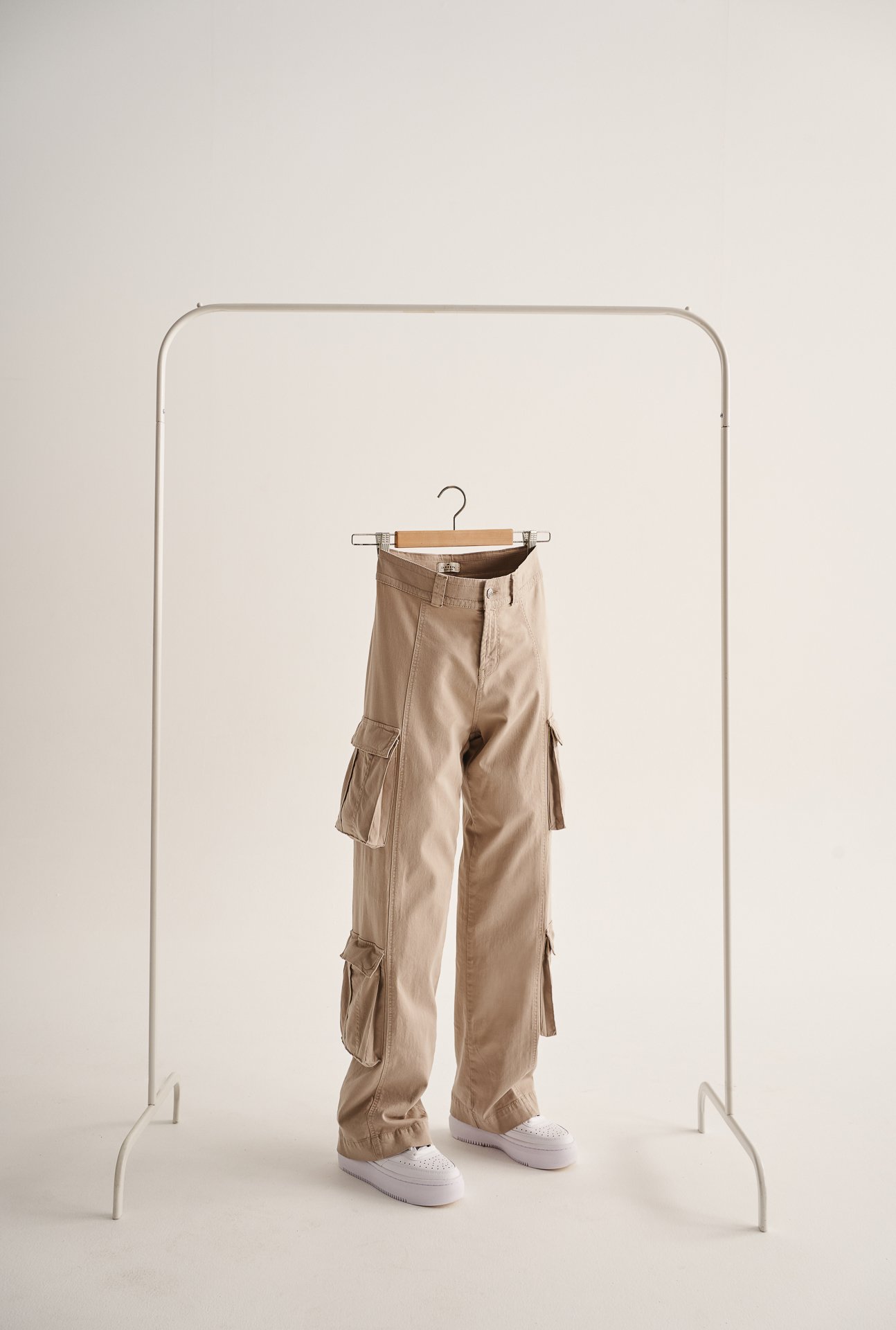 Paio di pantaloni beige con tasche cargo appesi a una gruccia in metallo
