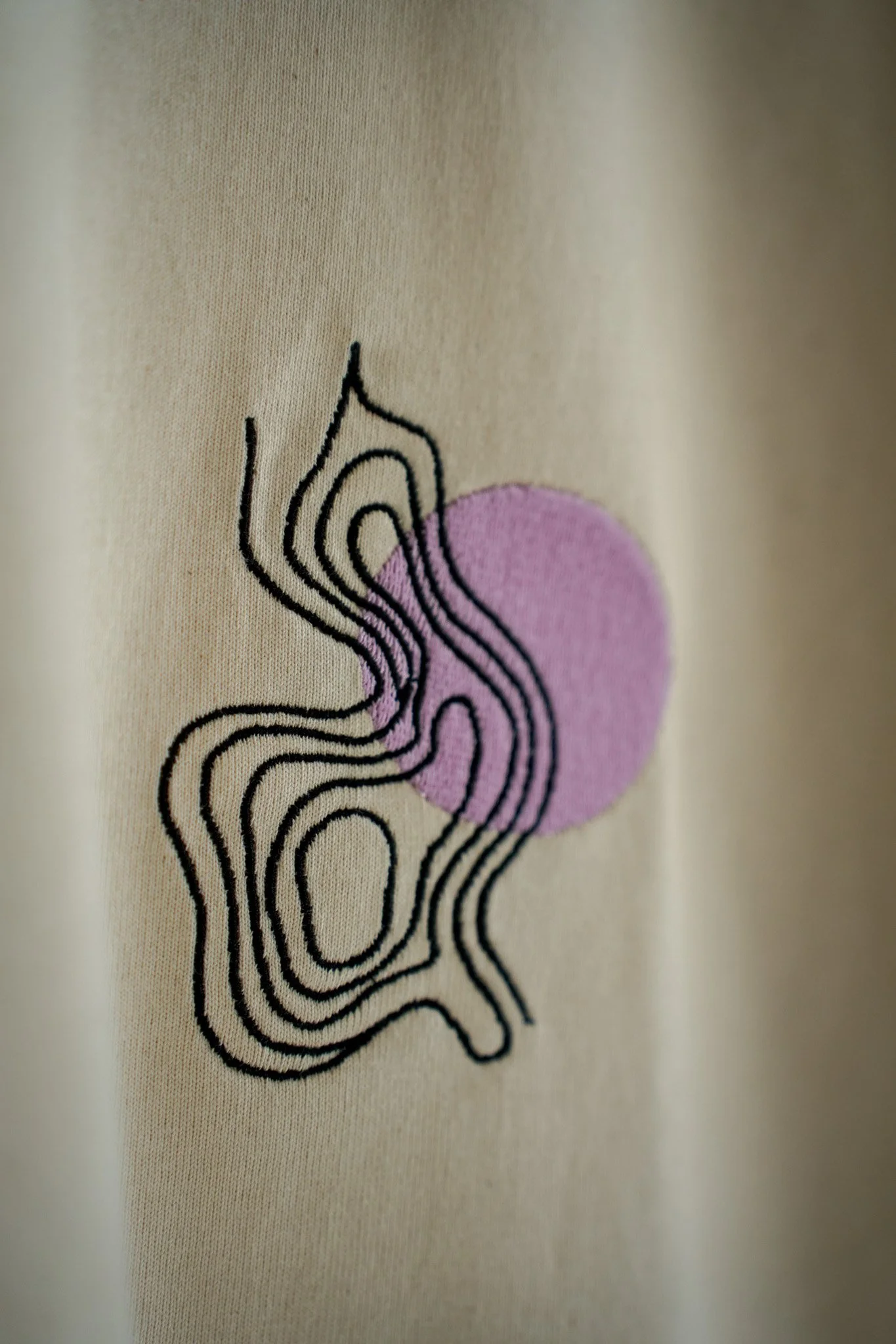 Close-up of a fabric with an embroidered abstract design featuring a purple circle and black wavy line patterns.