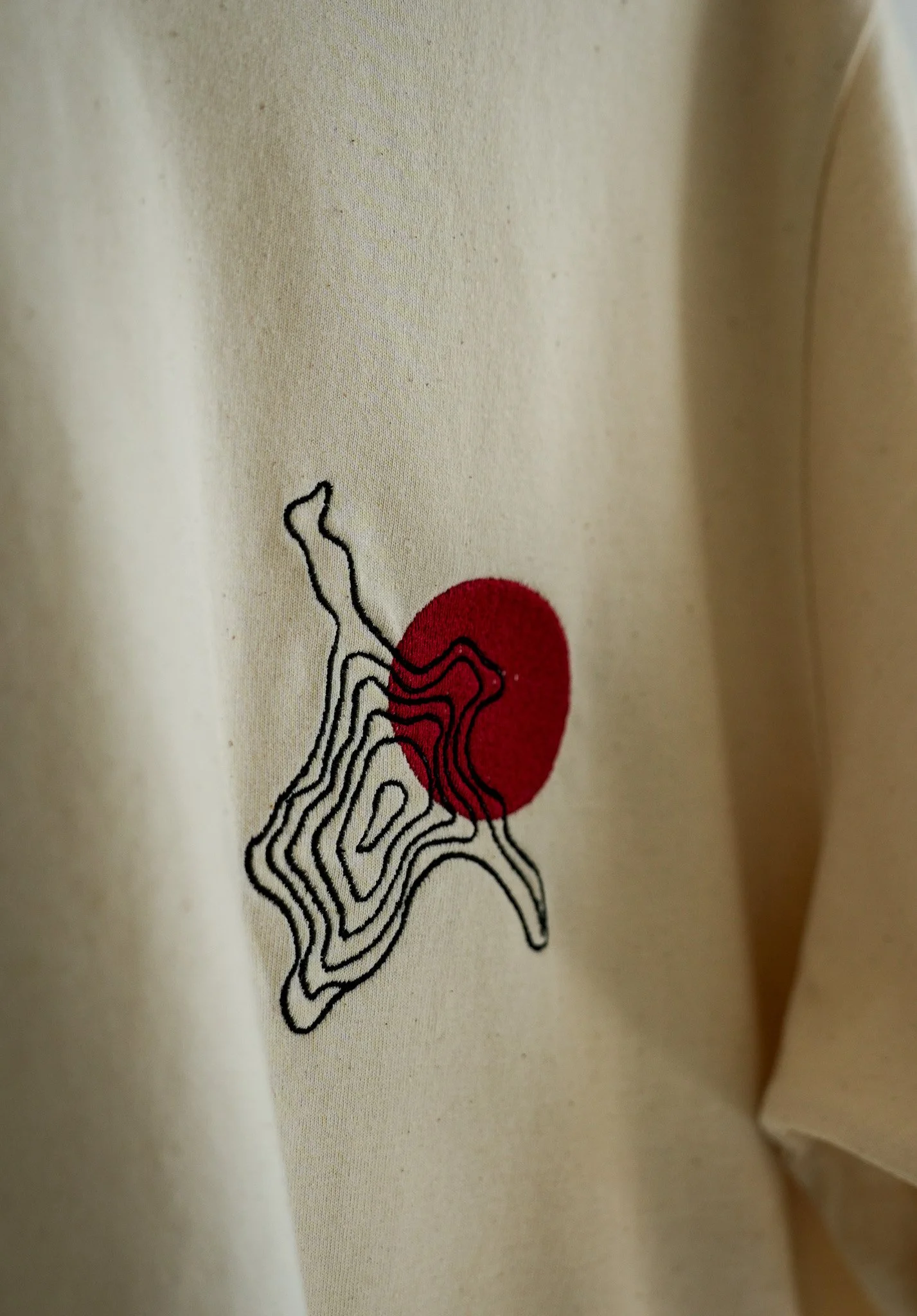 Close-up of a light-colored fabric with a design featuring a red circle and black contour lines.