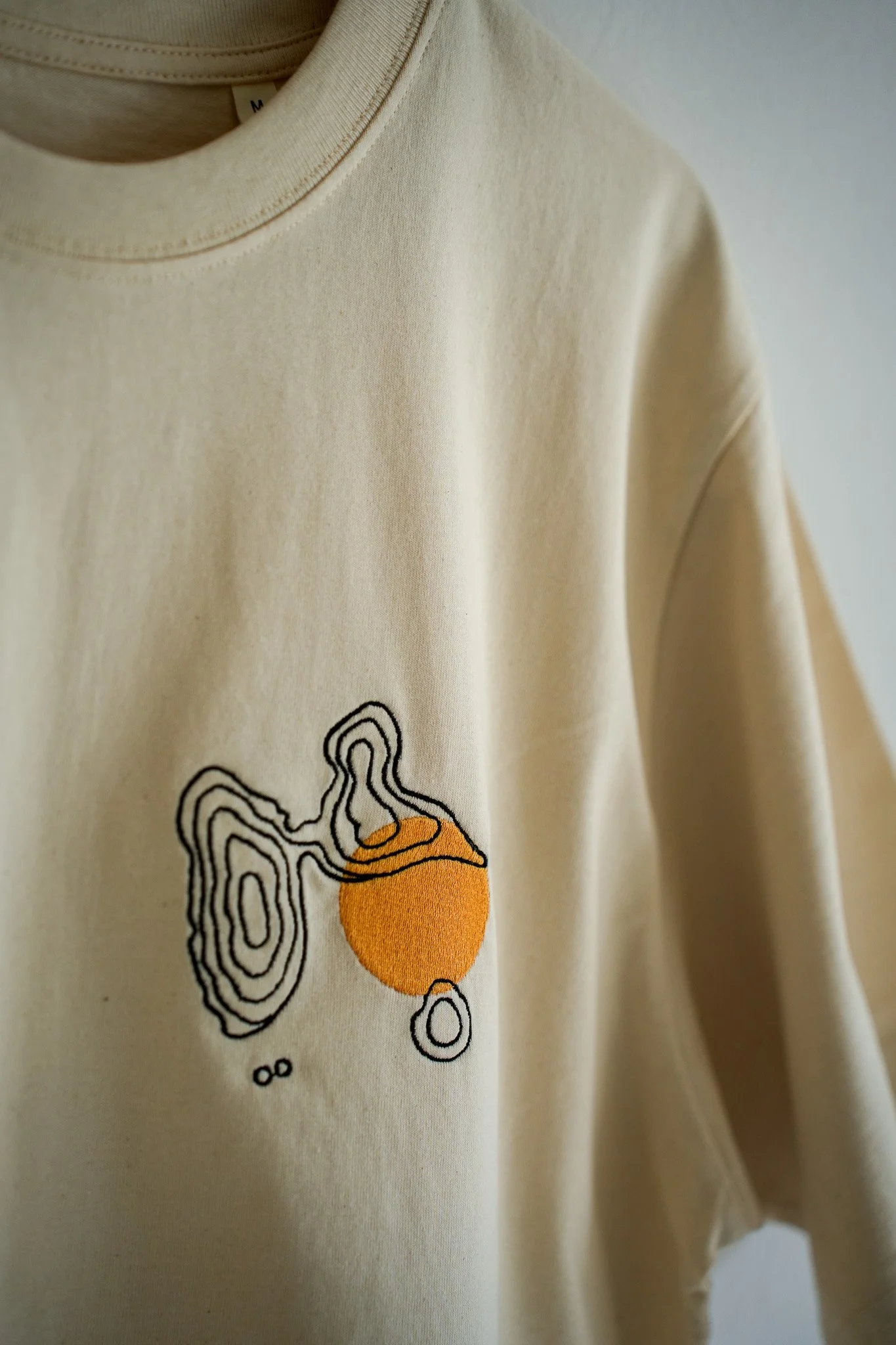 Beige sweatshirt with a black and orange abstract design on the front.