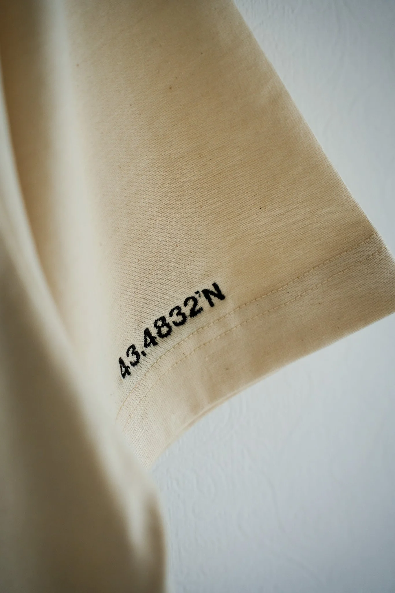 Close-up of a beige fabric with printed black text '43.44832'N' near the hem.