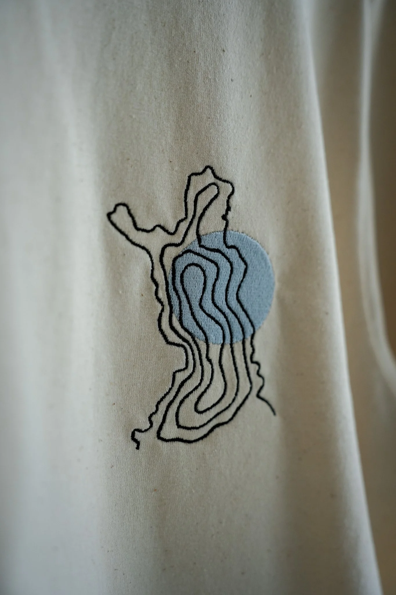 Close-up of a fabric with a design of black contour lines outlining a landmass, with a blue circle over part of the landmass.