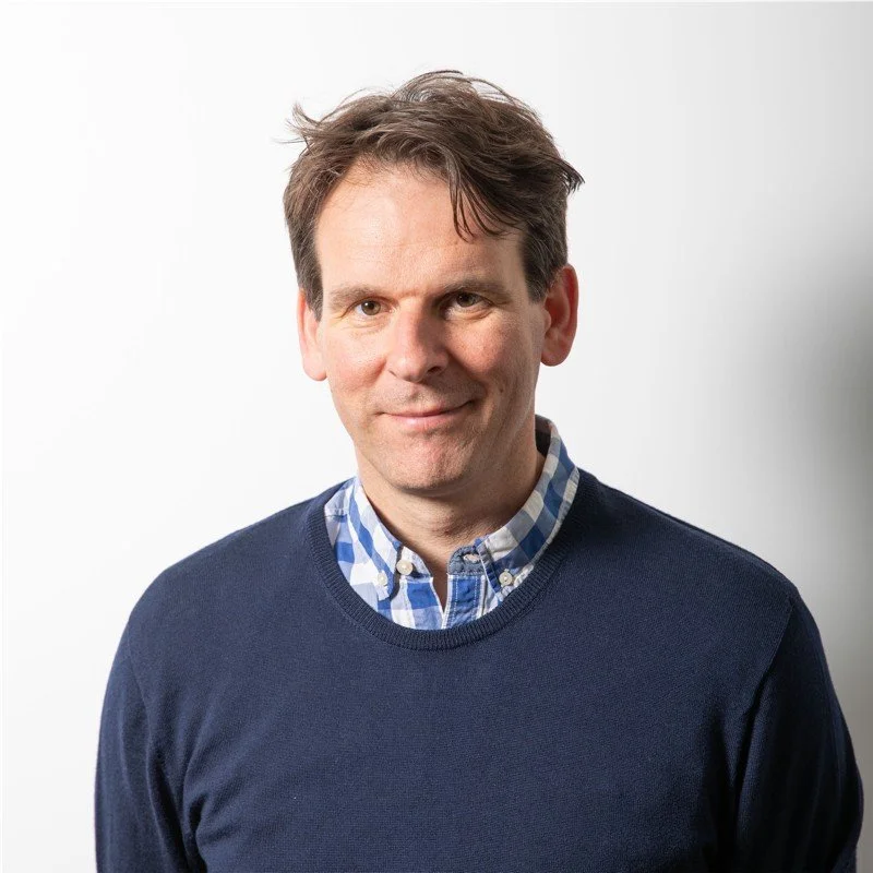 A man with short dark hair smiles to camera with a plain white background