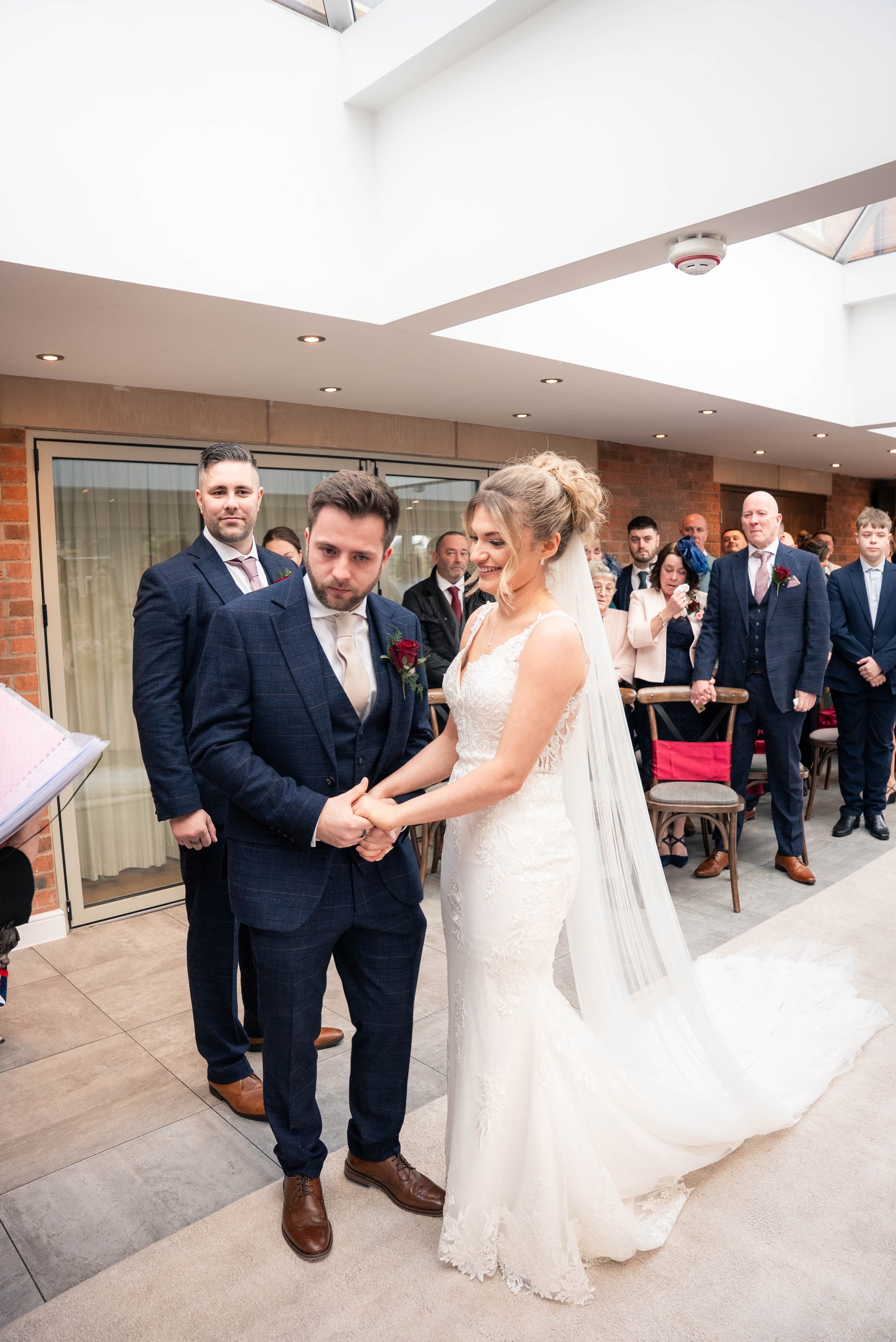 Bride and groom holding hands during their wedding ceremony, surrounded by friends and family.