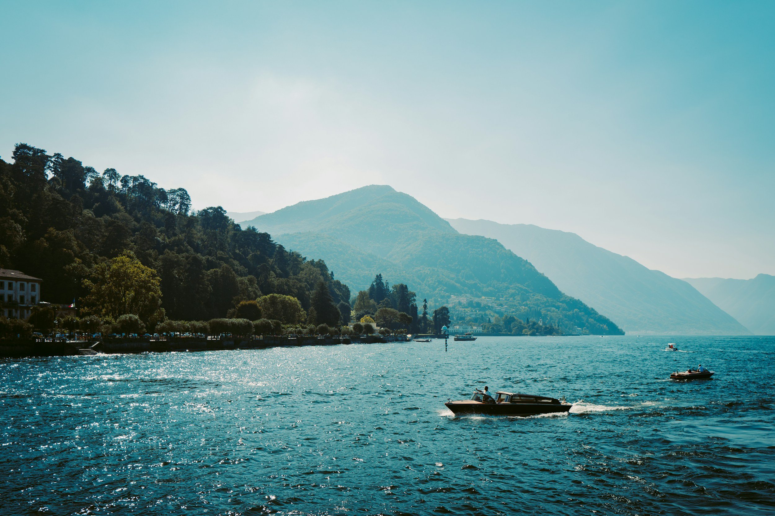 Boats on a large lake with mountains in the background and a clear sky.