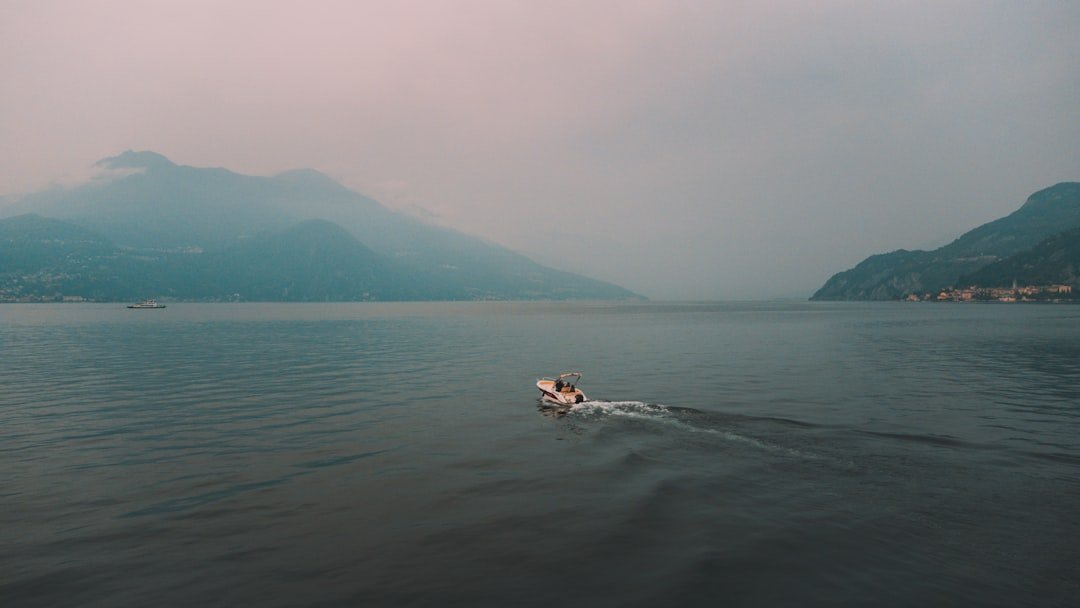 A boat moving across a calm lake surrounded by mountains under a cloudy sky.