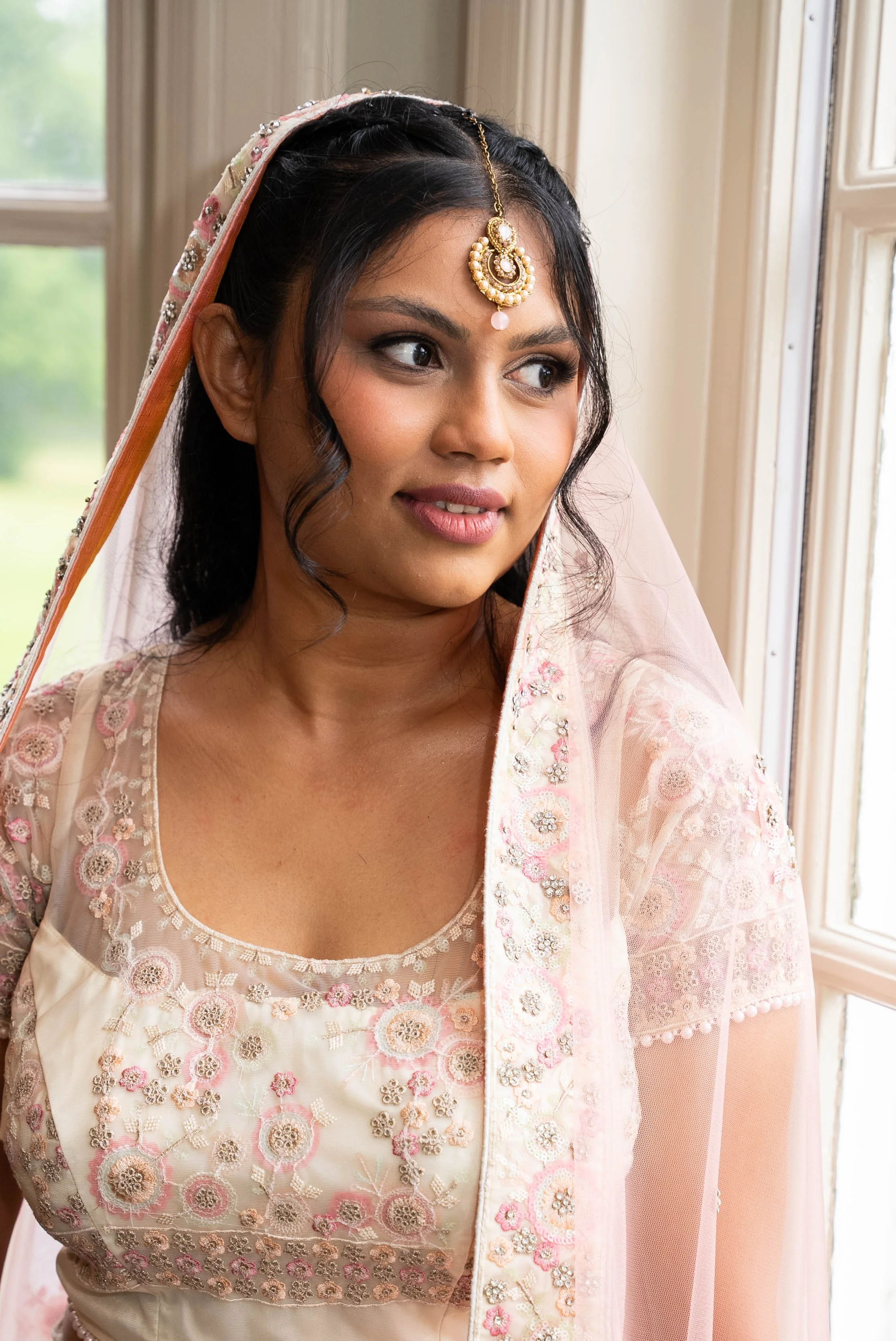 A woman dressed in traditional Indian attire looking out the window with a thoughtful expression.