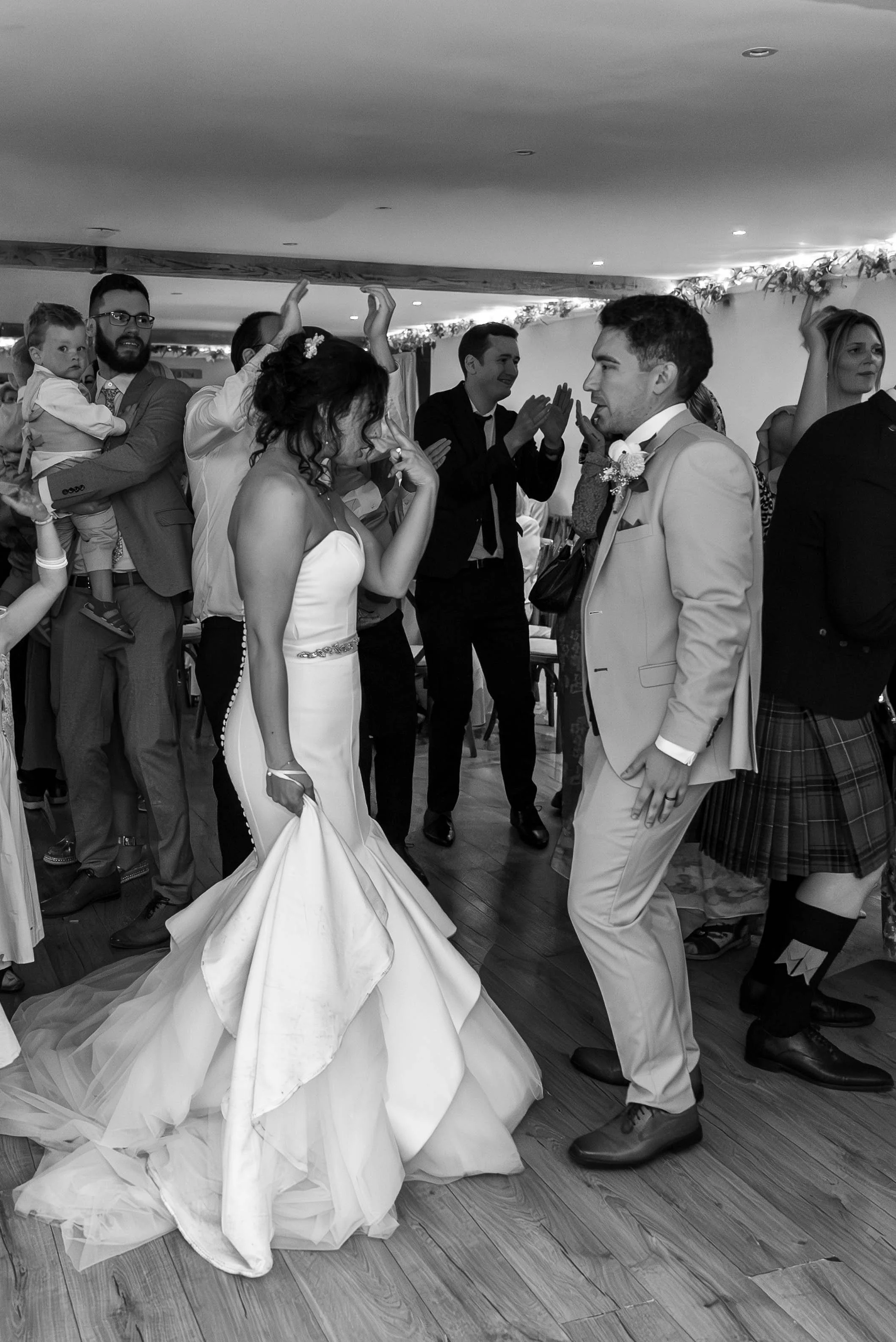 A bride and groom dancing at their wedding reception with guests surrounding them.