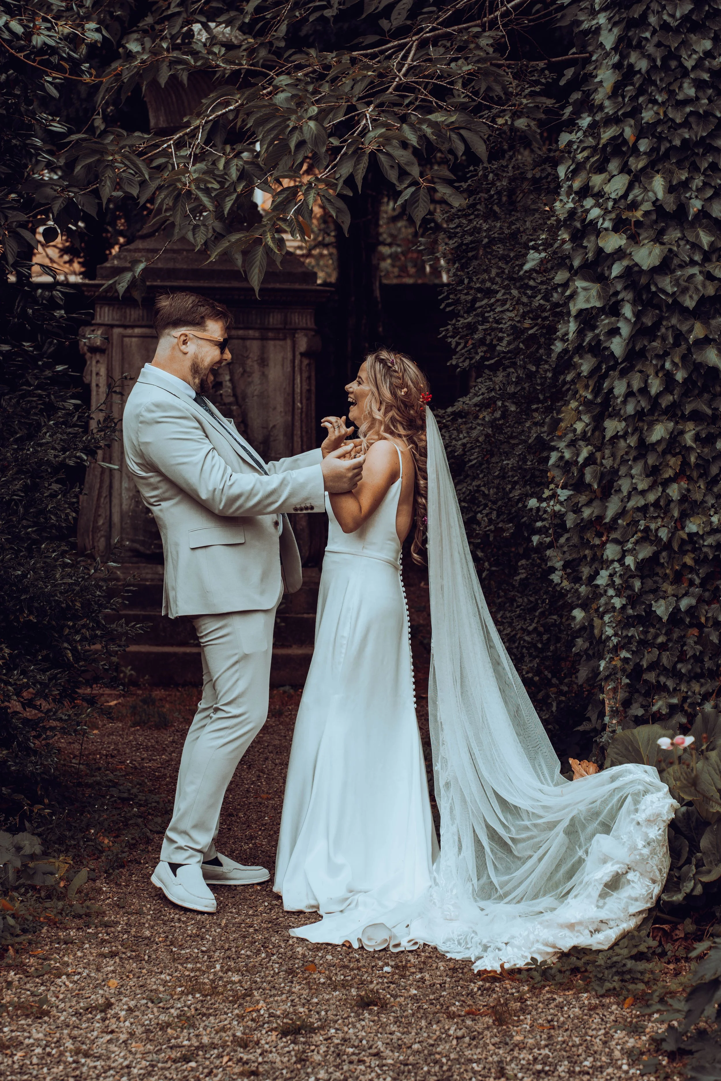A couple dressed in wedding attire sharing a joyful moment outdoors surrounded by greenery.