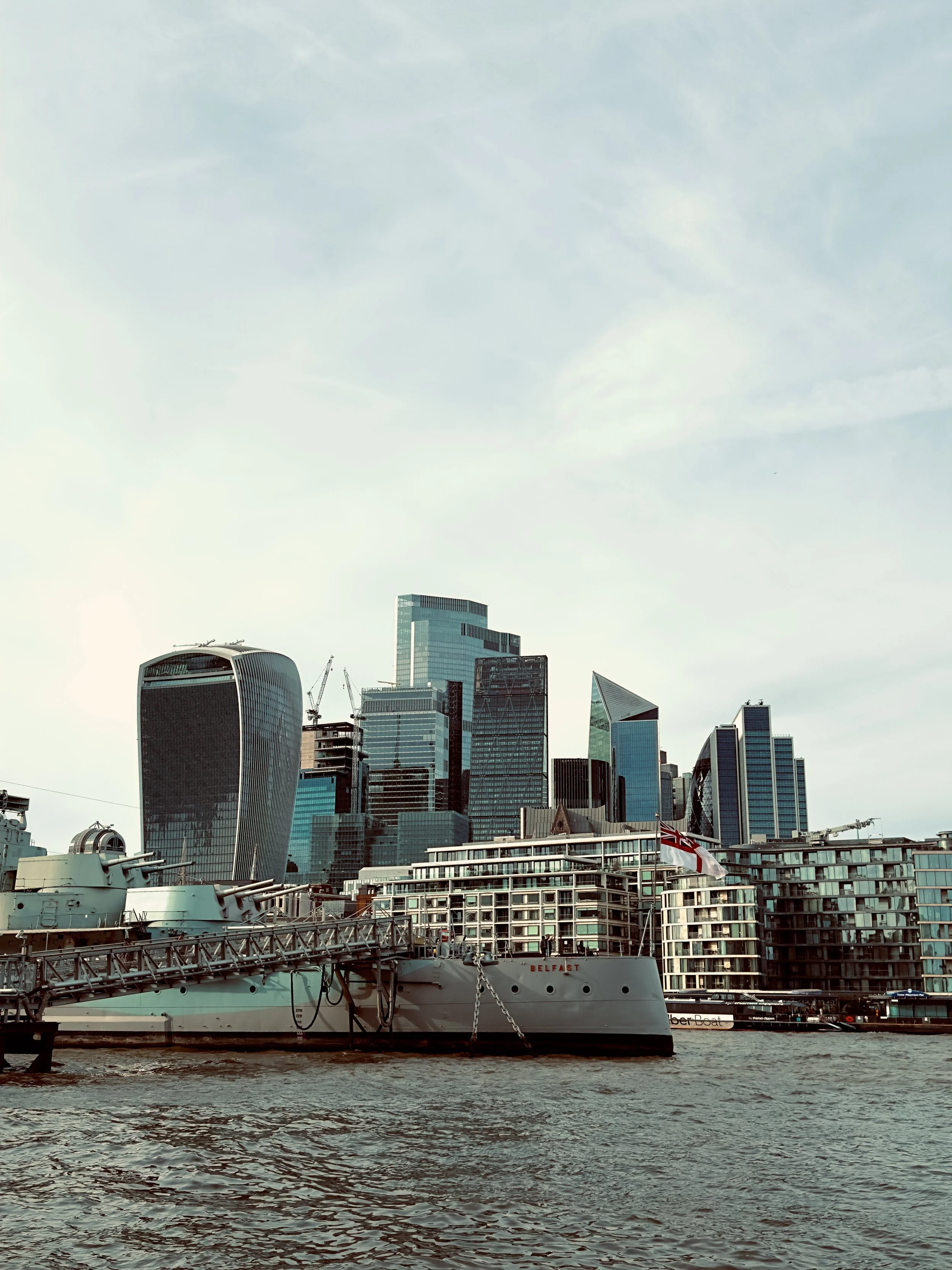London city skyline with modern skyscrapers viewed from the river, featuring a docked ship in the foreground.